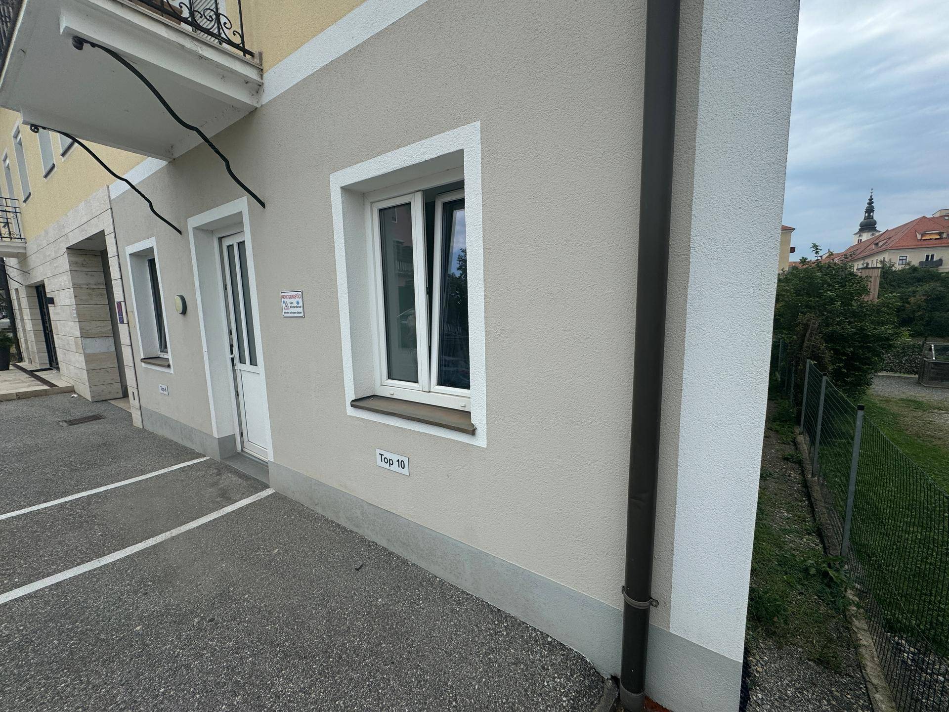 Parkplätze vor dem Gebäude mit einem Fenster und einem Fallrohr an der Fassade, gut gepflegt.