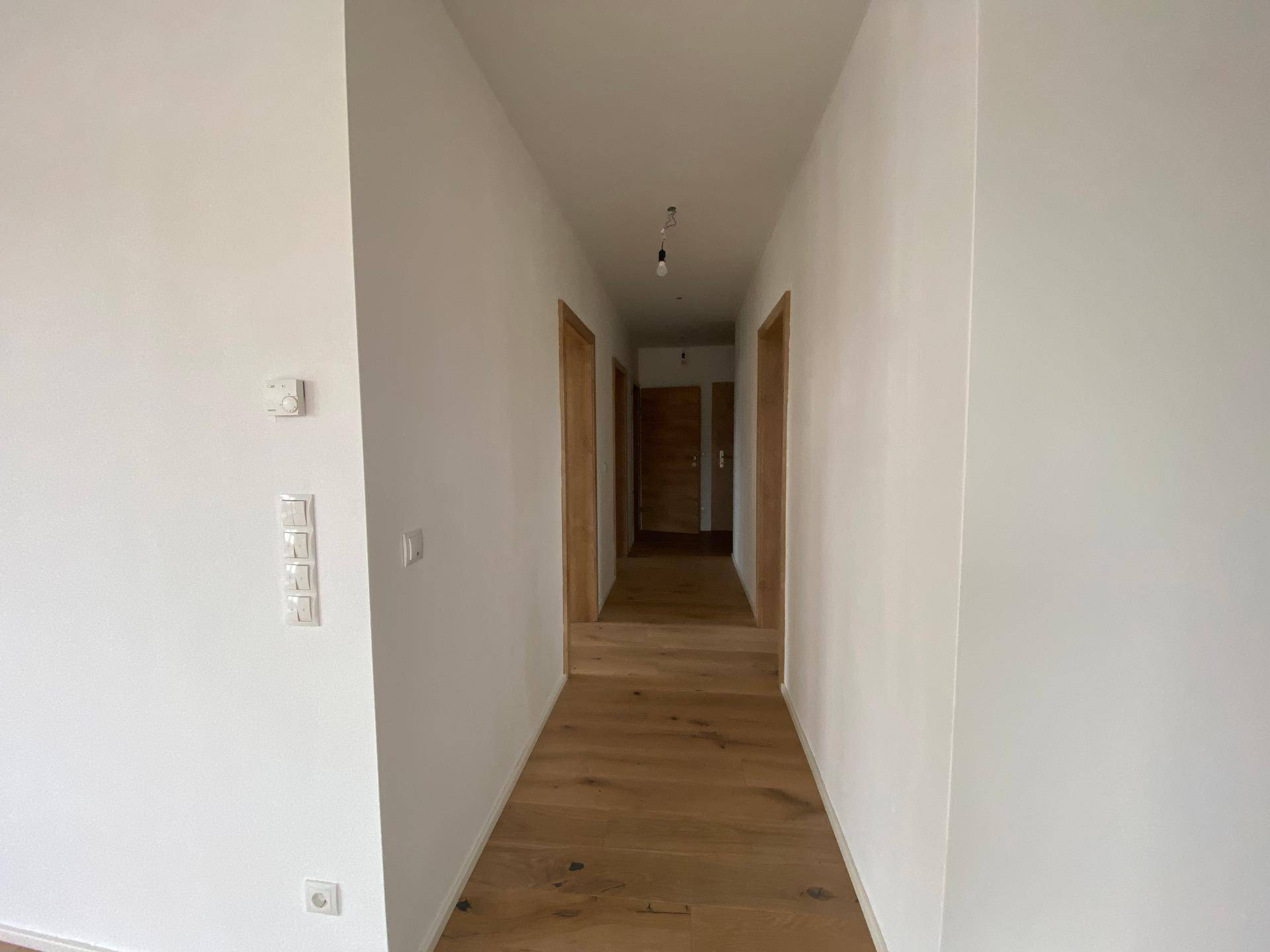 Langer, heller Flur mit Holzboden und mehreren Holztüren, die zu den Zimmern führen.