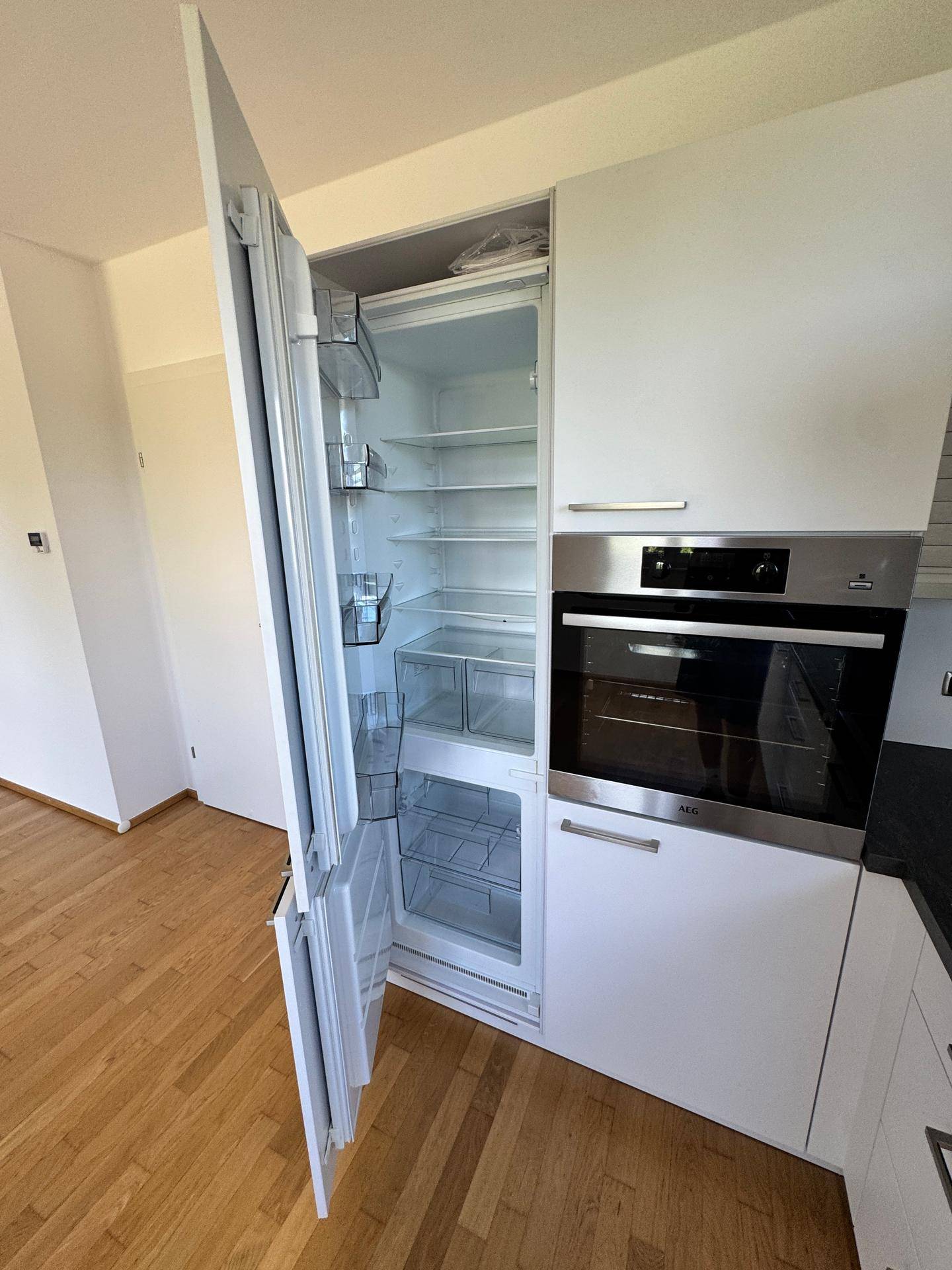 Integrierter Kühlschrank und Backofen der Marke AEG in einer modernen, weißen Einbauküche.