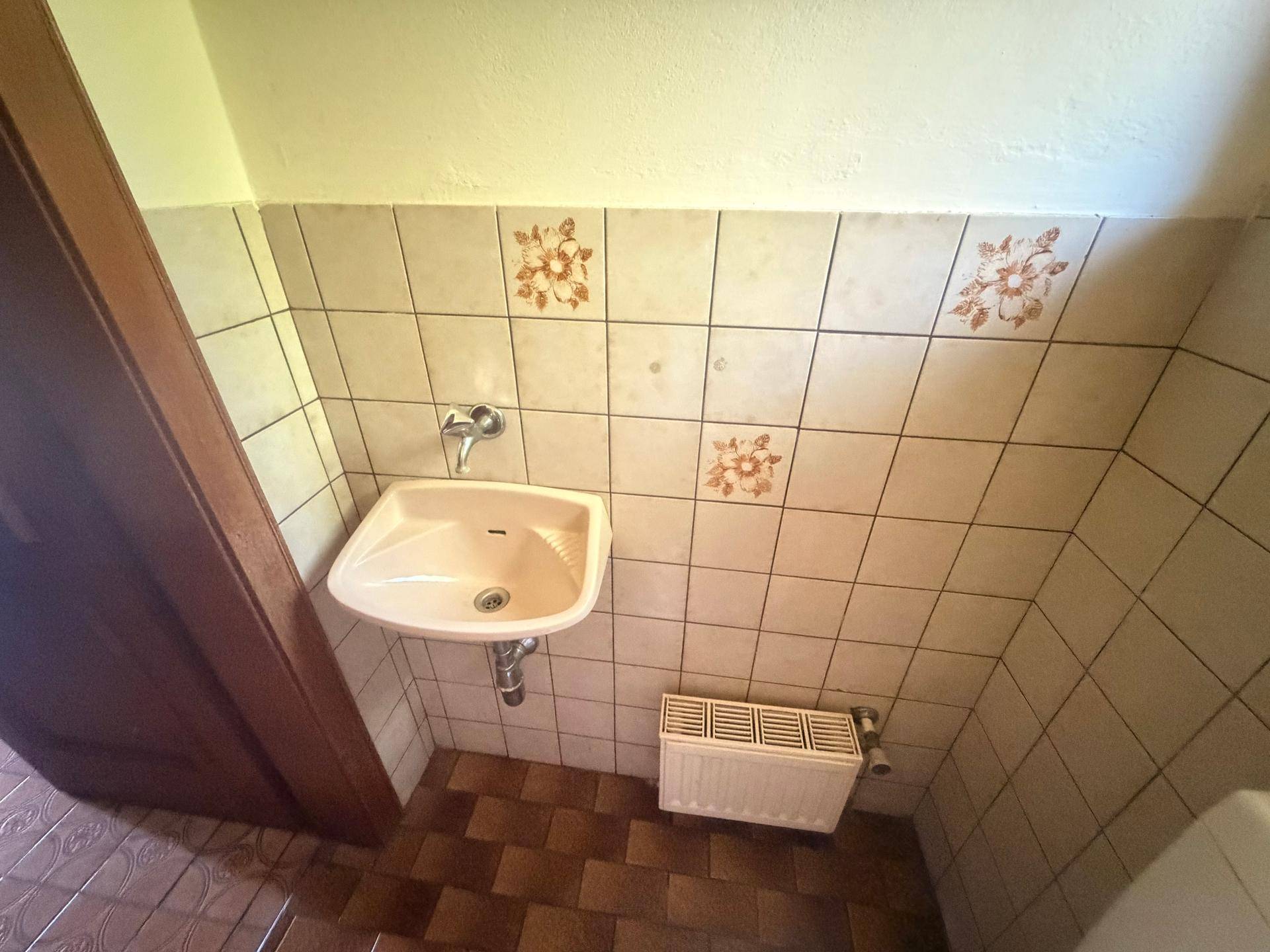 Kleine Gästetoilette mit Waschbecken, Fliesen und Heizkörper.