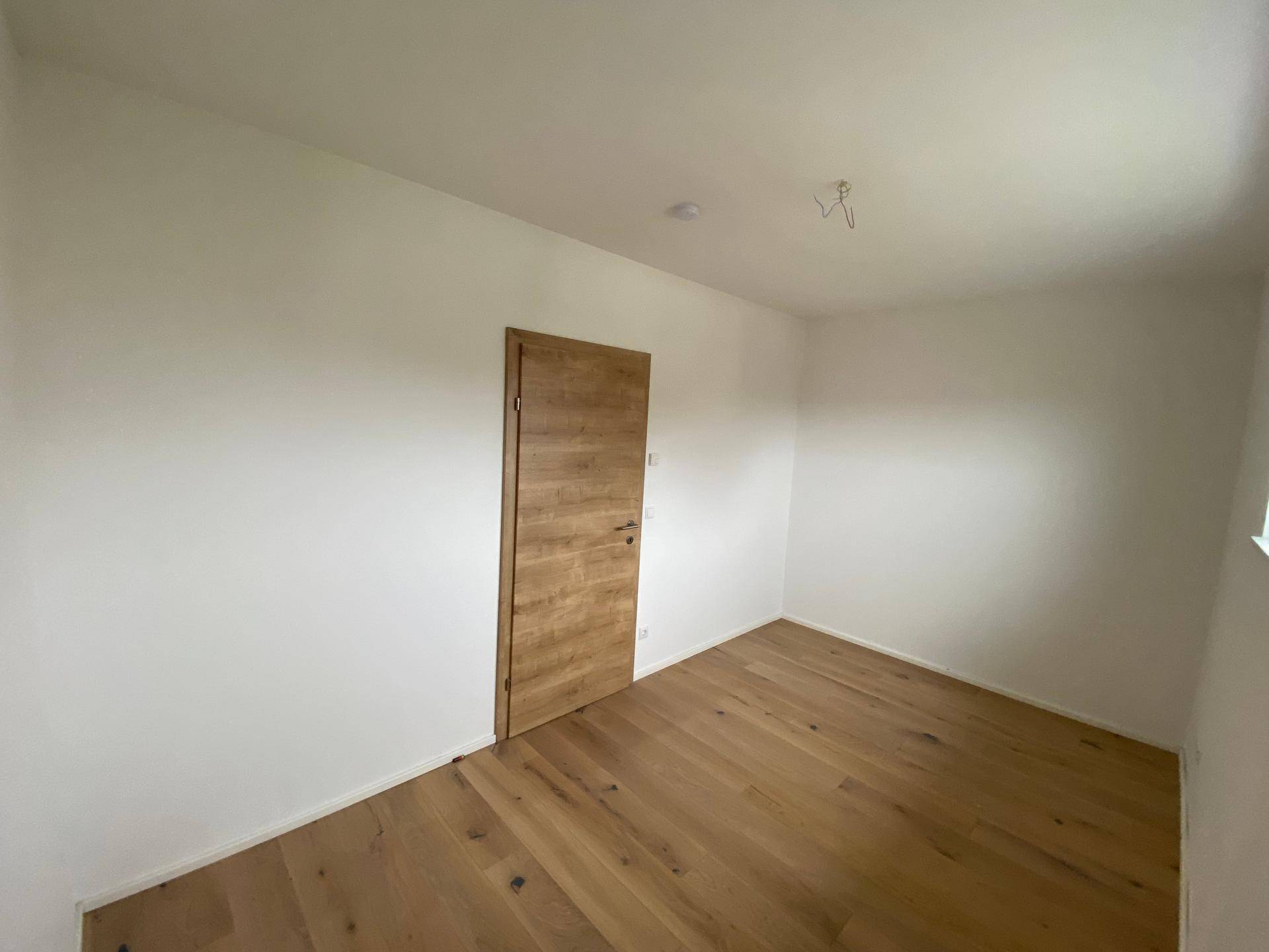 Geräumiges Schlafzimmer mit Holzboden und Holztür, bereit zur individuellen Gestaltung.