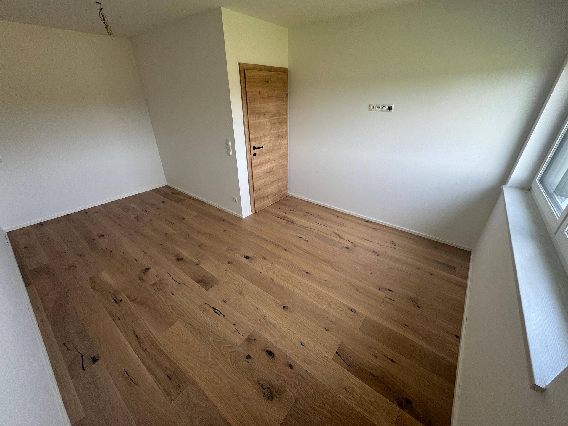 Schlafzimmer mit hellem Eichenparkett, weißen Wänden und Fenster.