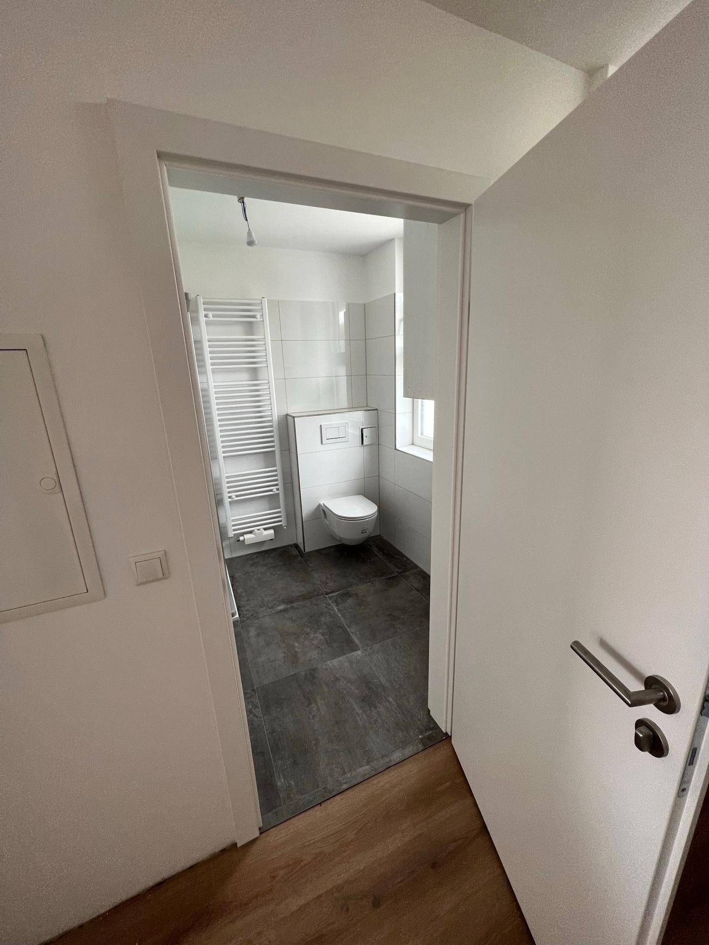 Eingang zu einem hellen Badezimmer mit modernen Fliesen, Dusche und wandhängendem WC.