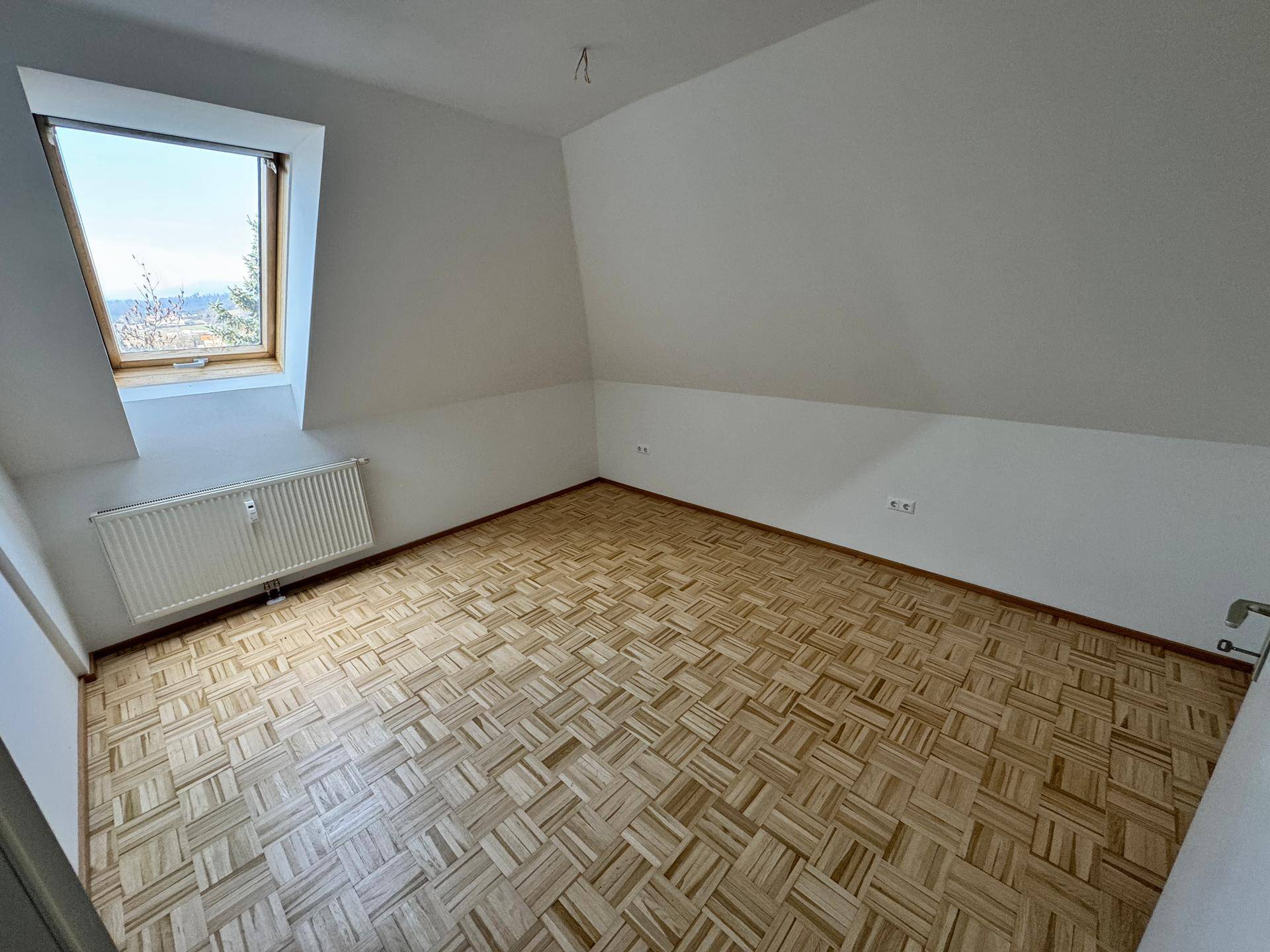 Helles Schlafzimmer im Dachgeschoss mit Parkettboden, Dachfenster und Heizkörper.