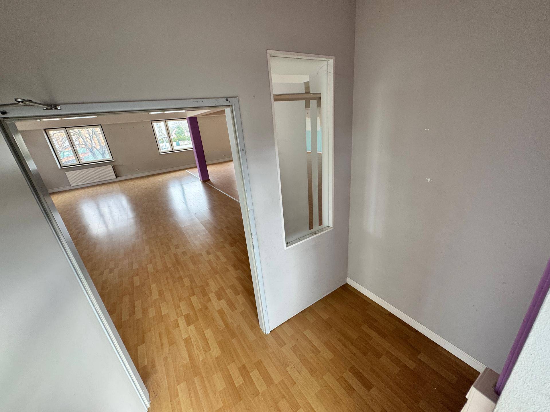 Eingangsbereich mit hellem Laminatboden, einer weißen Tür und Blick in einen größeren Raum.