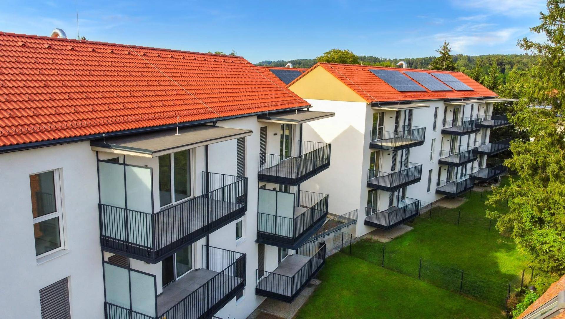 Moderner Wohnkomplex mit weißen Fassaden, roten Ziegeldächern, Balkonen und Photovoltaikanlagen.