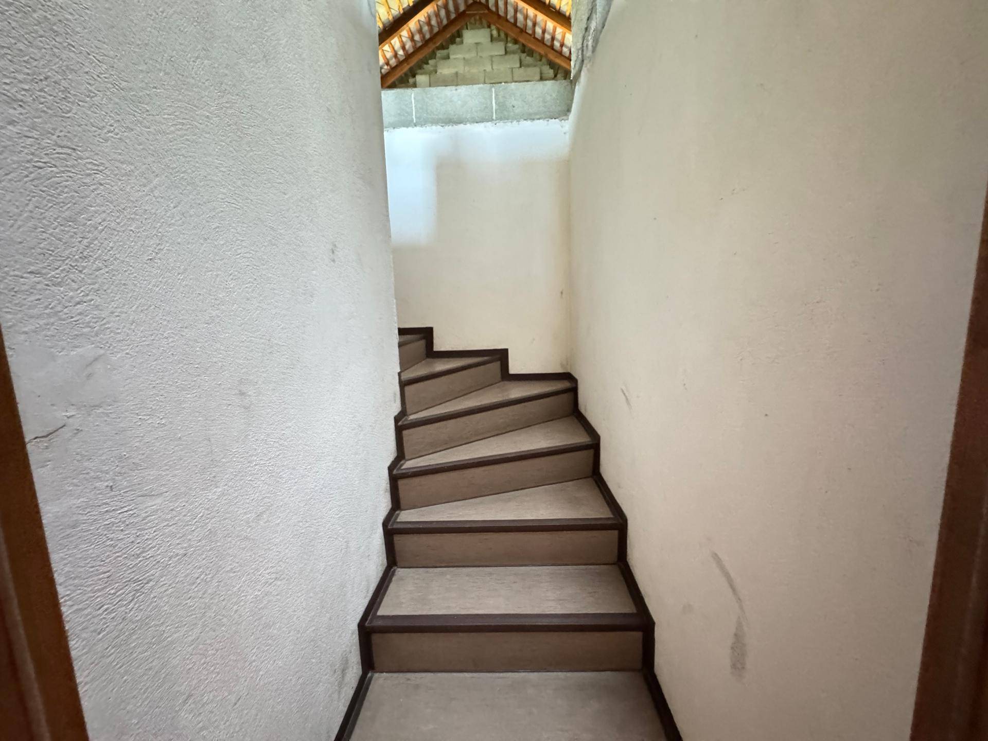 Treppenaufgang mit rohen Wänden und sichtbarer Dachkonstruktion, der in das Obergeschoss führt.