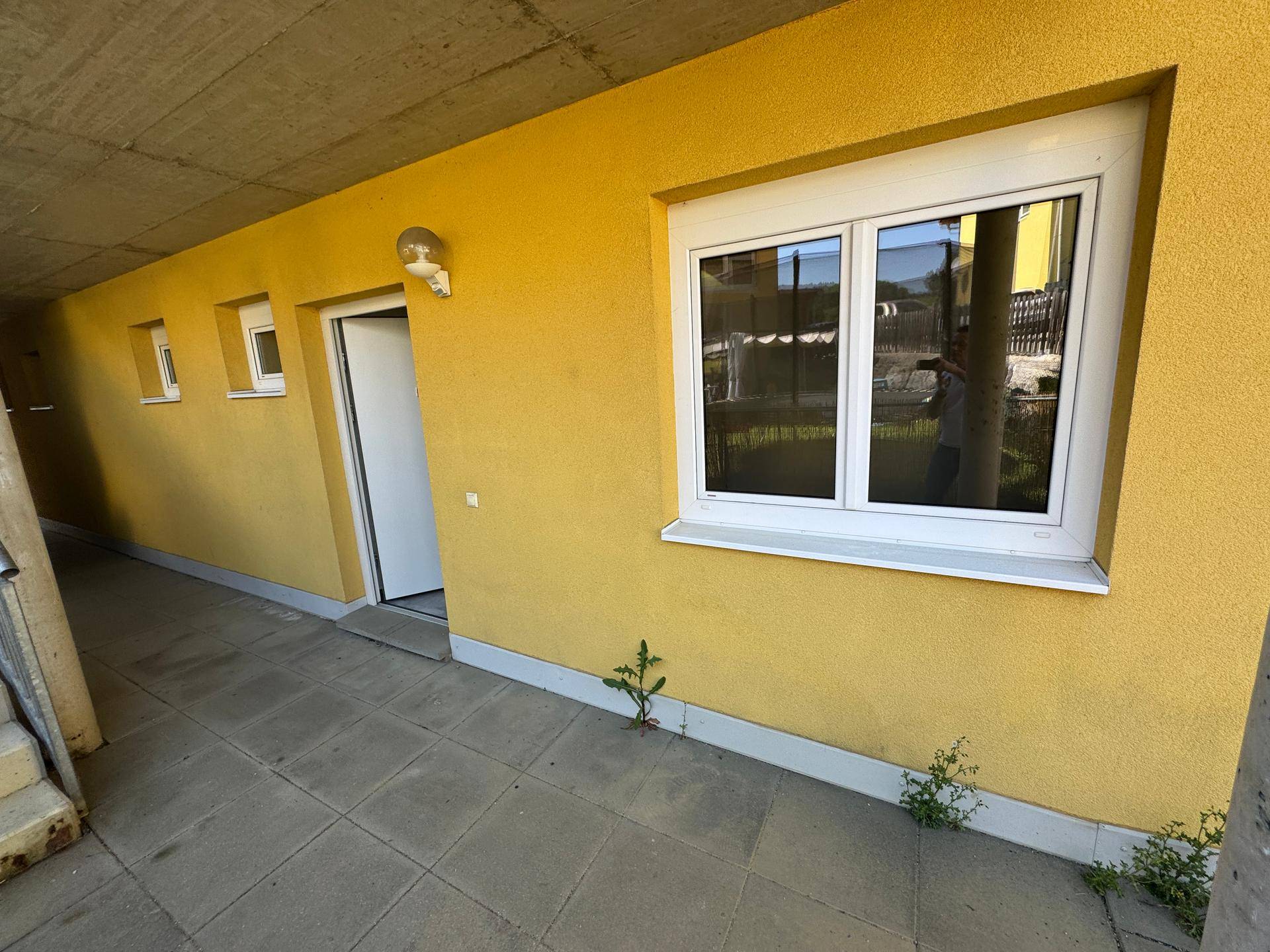 Überdachter Bereich mit gelber Wand, Fenster und Tür unter einem Betonüberbau.