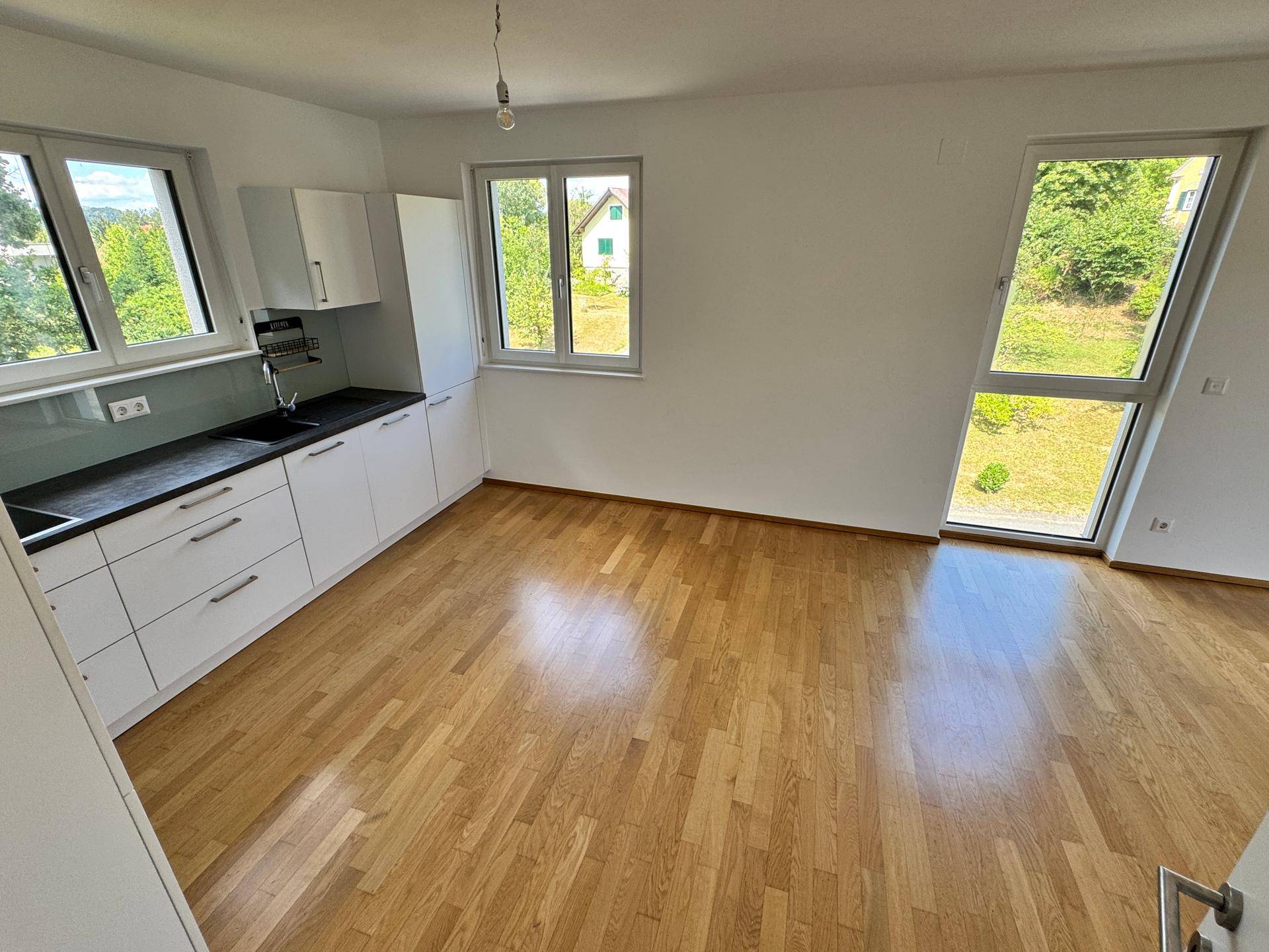 Moderne Küche mit weißen Schränken und Holzboden, integriert in einen hellen Raum mit großen Fenstern.