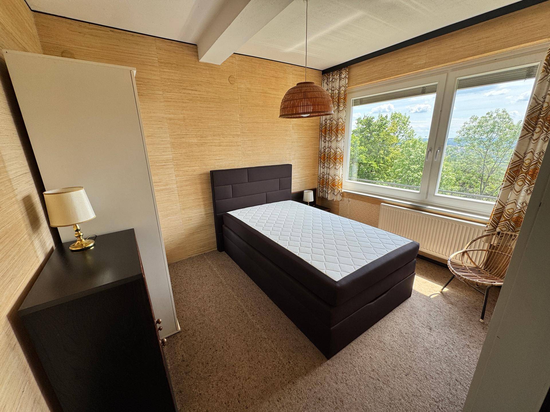 Schlafzimmer mit Teppichboden, Doppelbett und Fenster mit Blick ins Grüne.