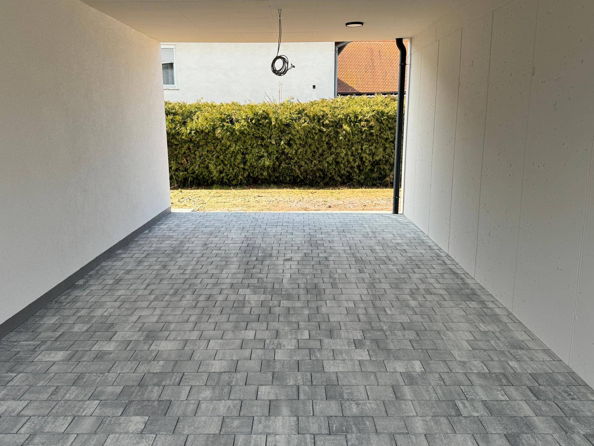 Geräumiger Carport mit gepflastertem Boden und Blick auf den hinteren Gartenbereich.