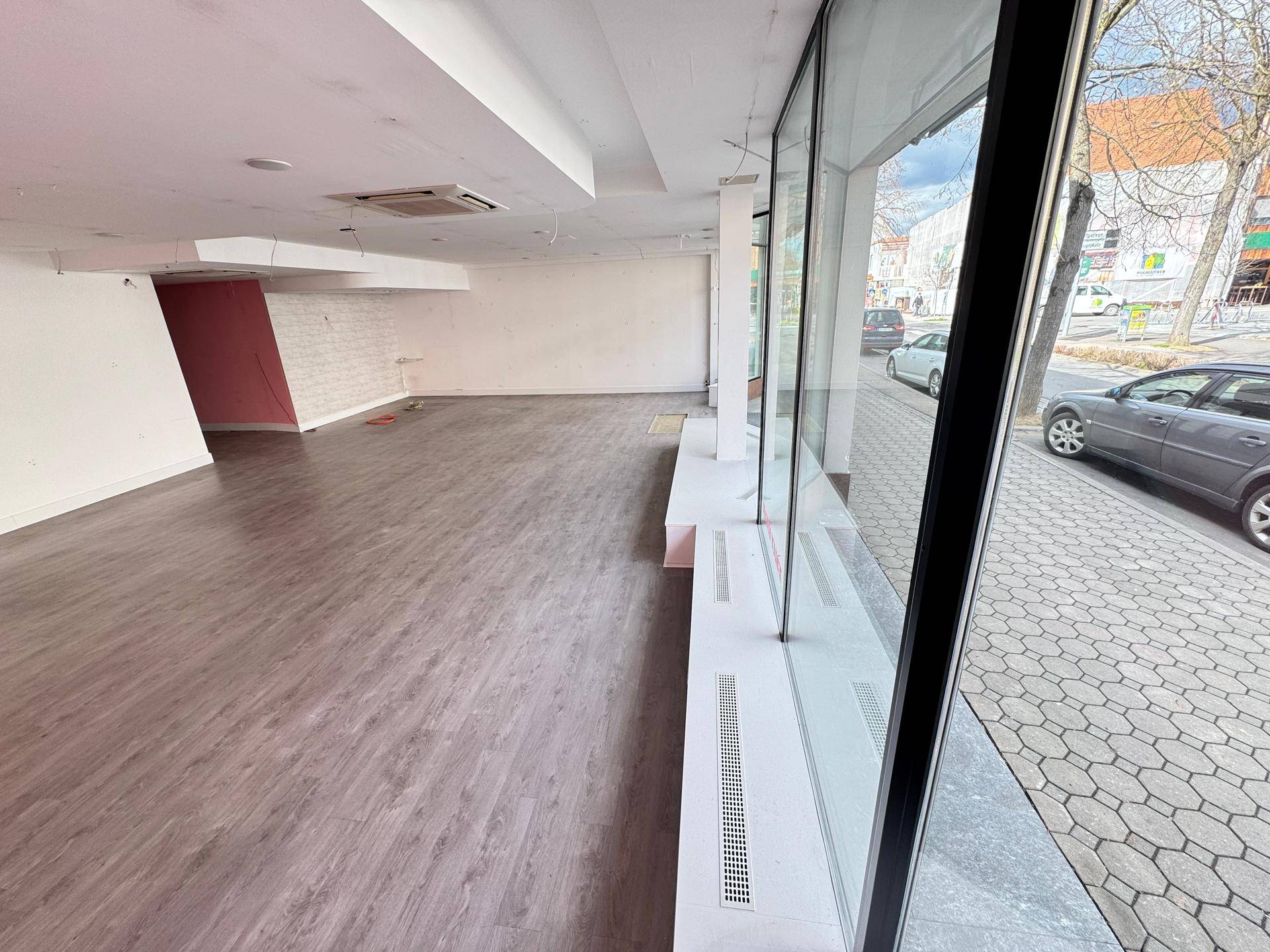 Geräumiger Innenraum des Geschäfts mit Laminatboden und großen Fenstern zur Straße.