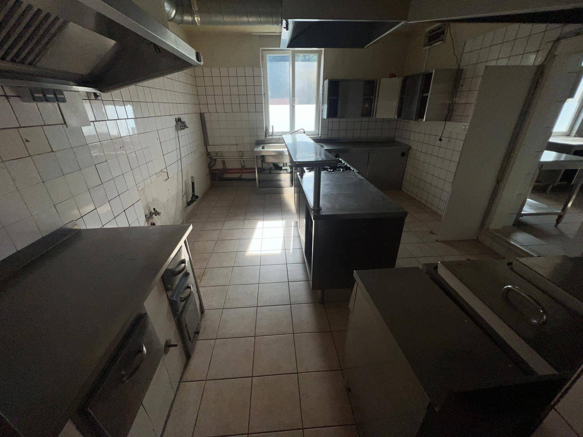 Geräumige Industrieküche mit Edelstahlgeräten, Fliesenwänden und großem Fenster für Tageslicht.