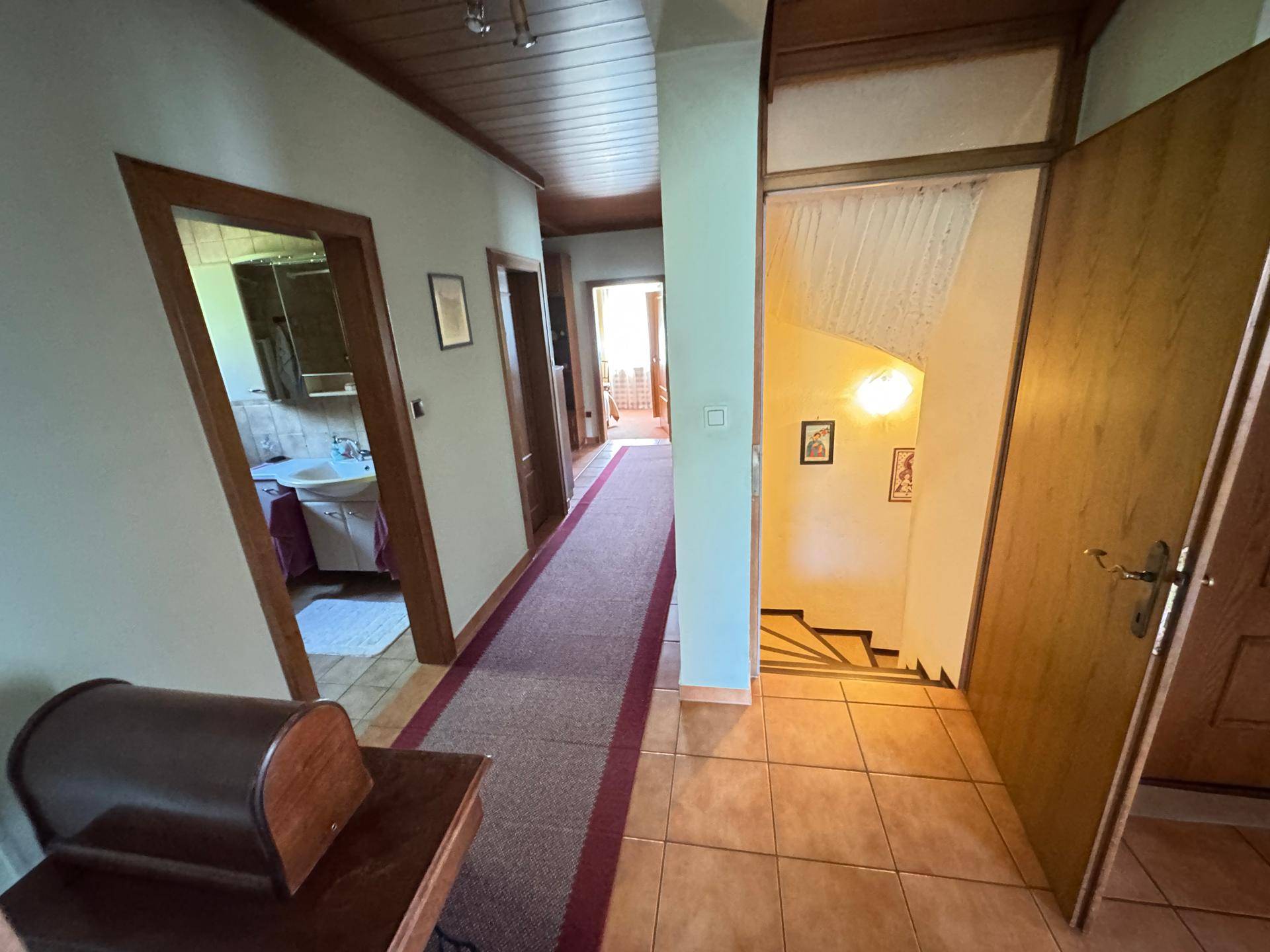 Langer Flur mit Fliesenboden, Holzdecke und Zugang zu verschiedenen Zimmern, inklusive Badezimmer.