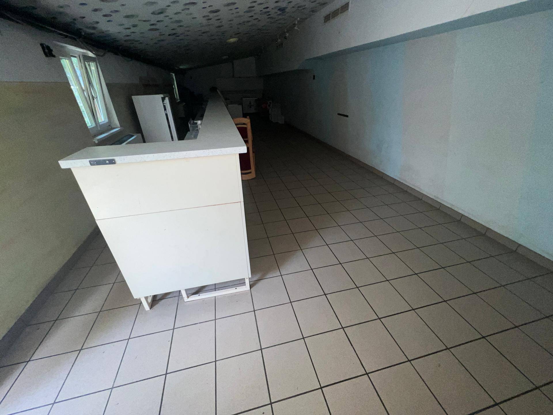 Langer, gefliester Raum mit einer Theke und dunkler Decke, möglicherweise ein Lagerbereich.