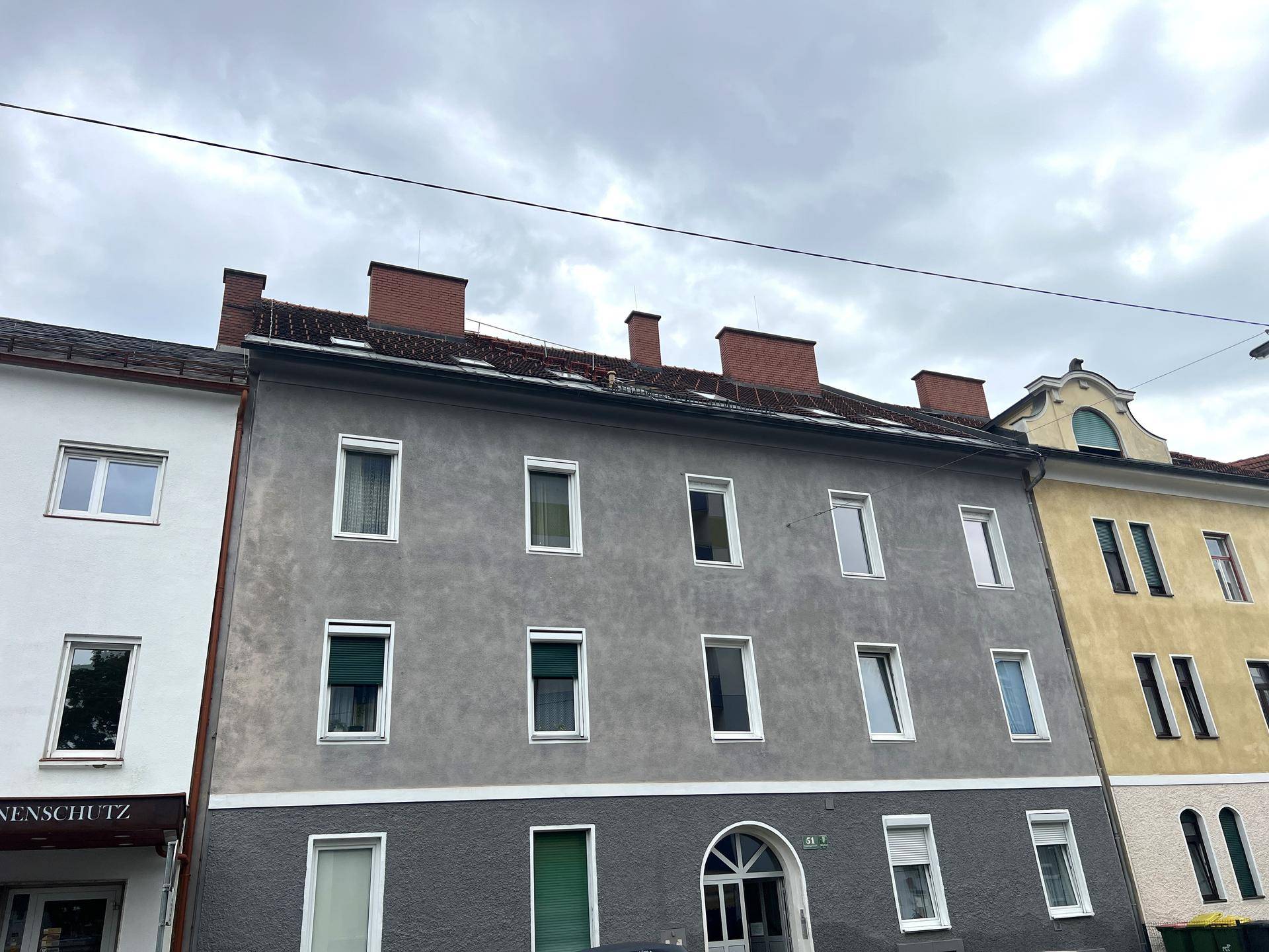 Graue Fassade eines Mehrfamilienhauses mit vielen Fenstern und traditioneller Architektur.