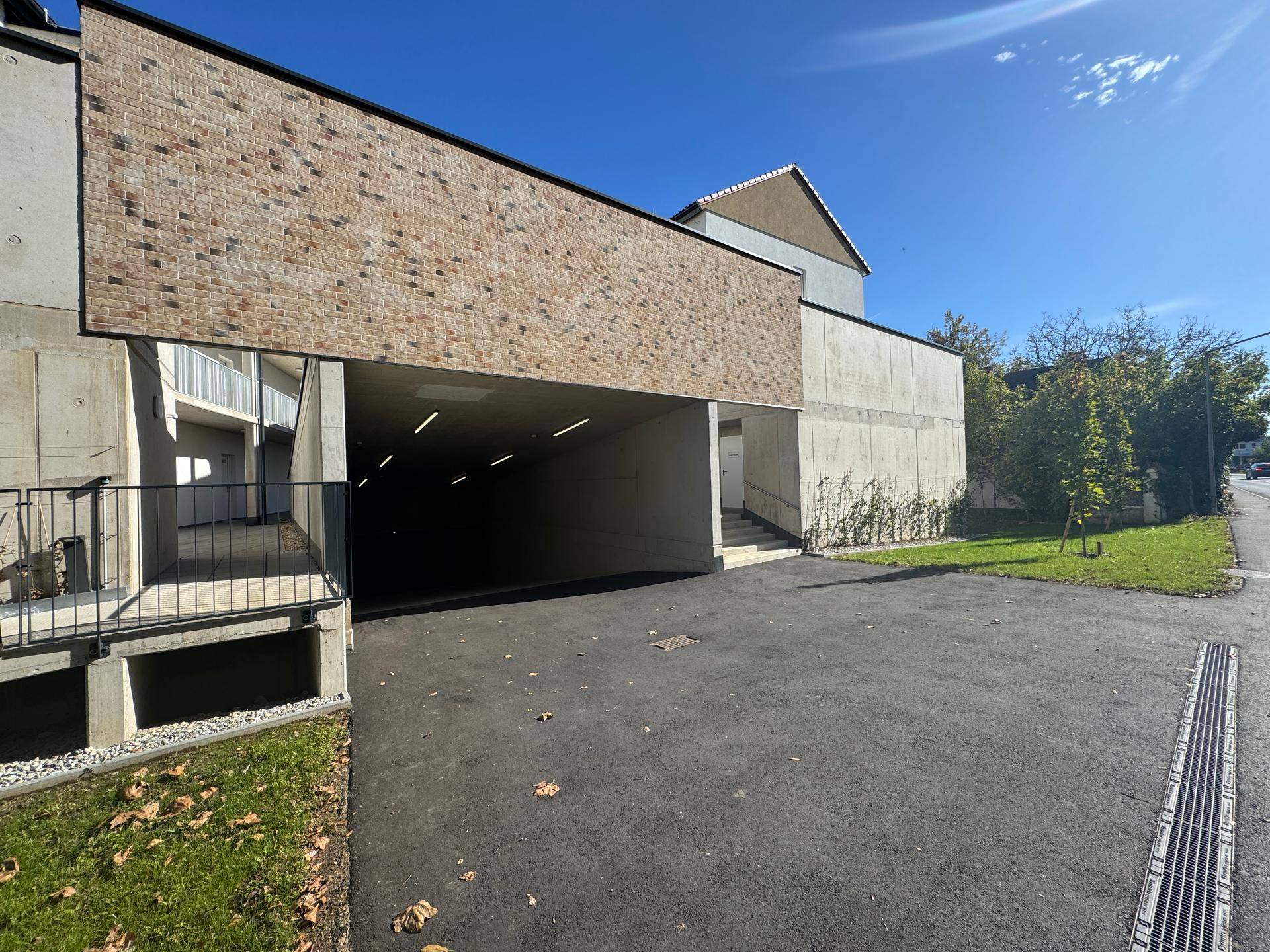 Zufahrt zur Tiefgarage mit Ziegelmauerwerk und asphaltiertem Vorplatz.