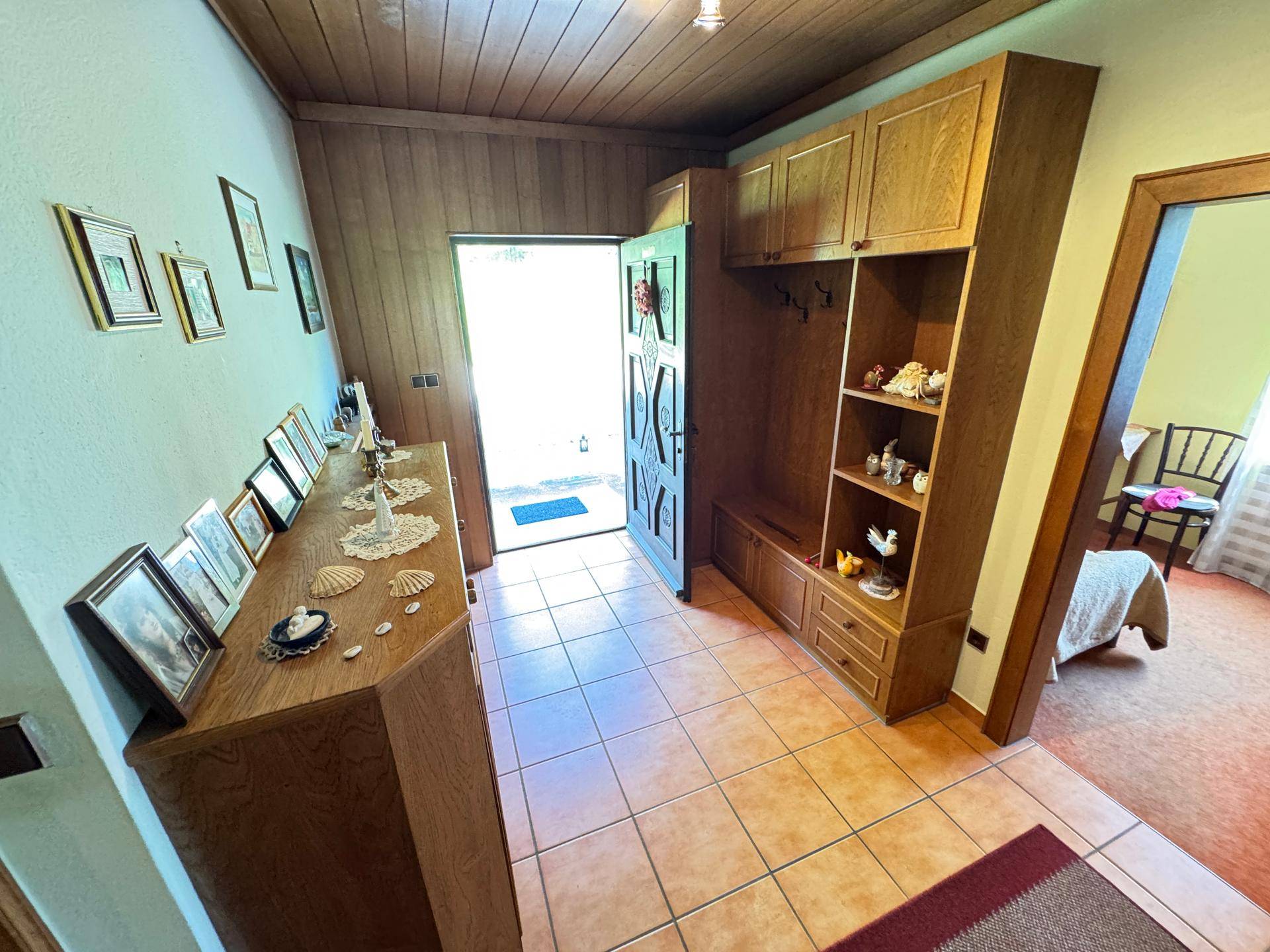 Eingangsbereich mit Fliesenboden, Holzdecke und einer Garderobe aus Holz mit Stauraum.
