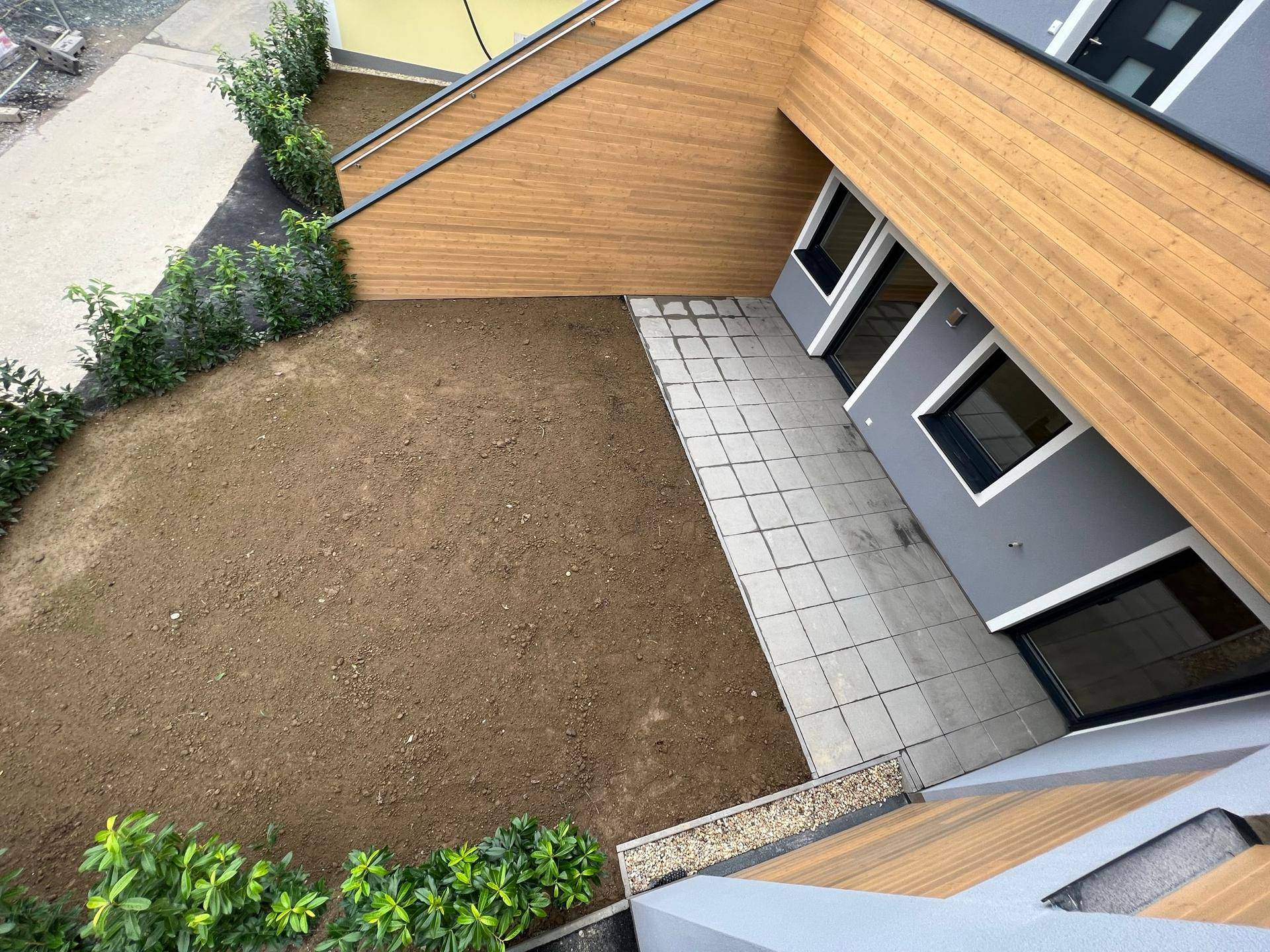 Außenbereich mit gepflasterter Terrasse und Rasenfläche, bereit zur individuellen Bepflanzung.