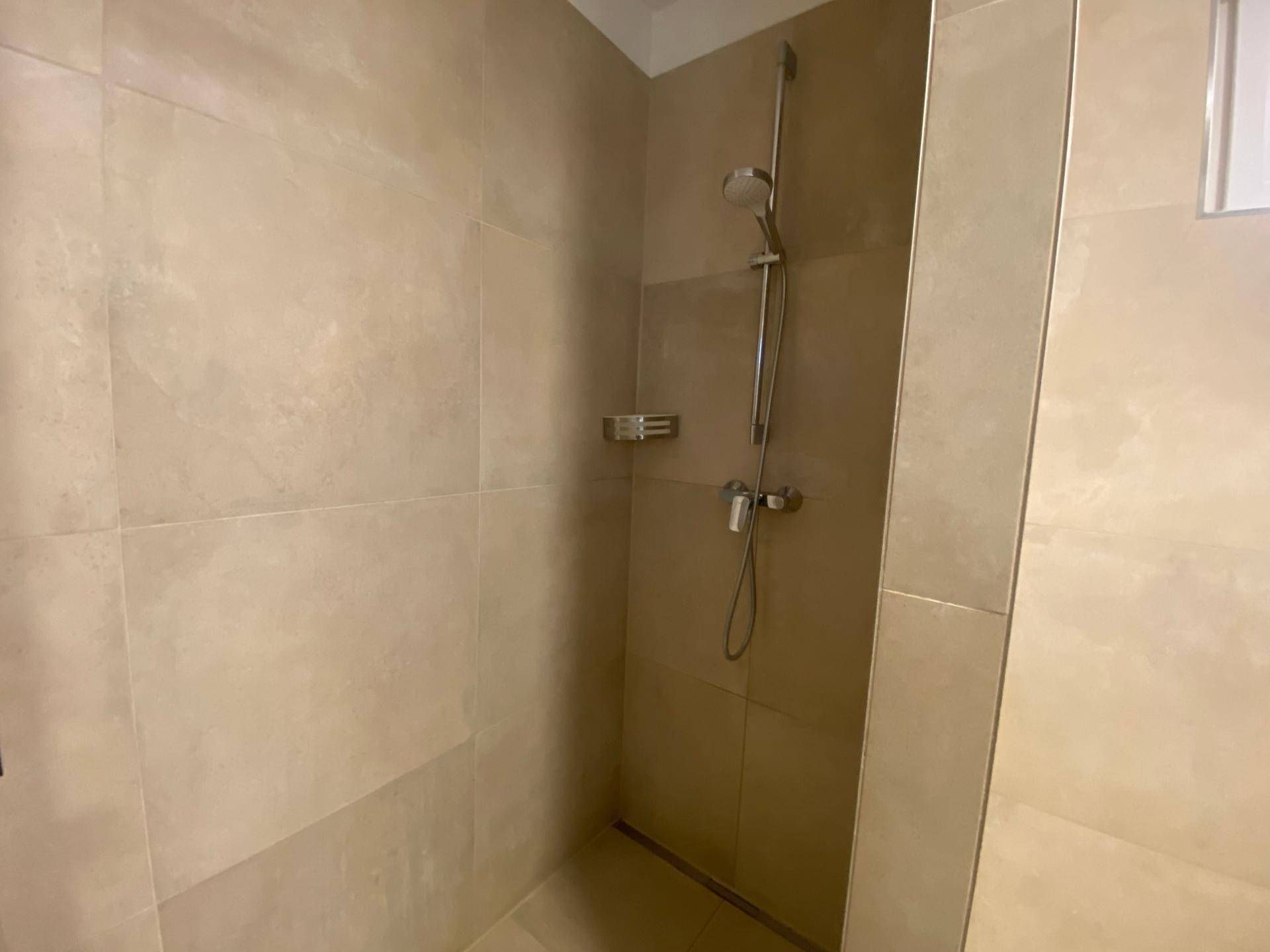 Ebenerdige Dusche im modernen Badezimmer mit beigefarbenen Fliesen und Duscharmatur.