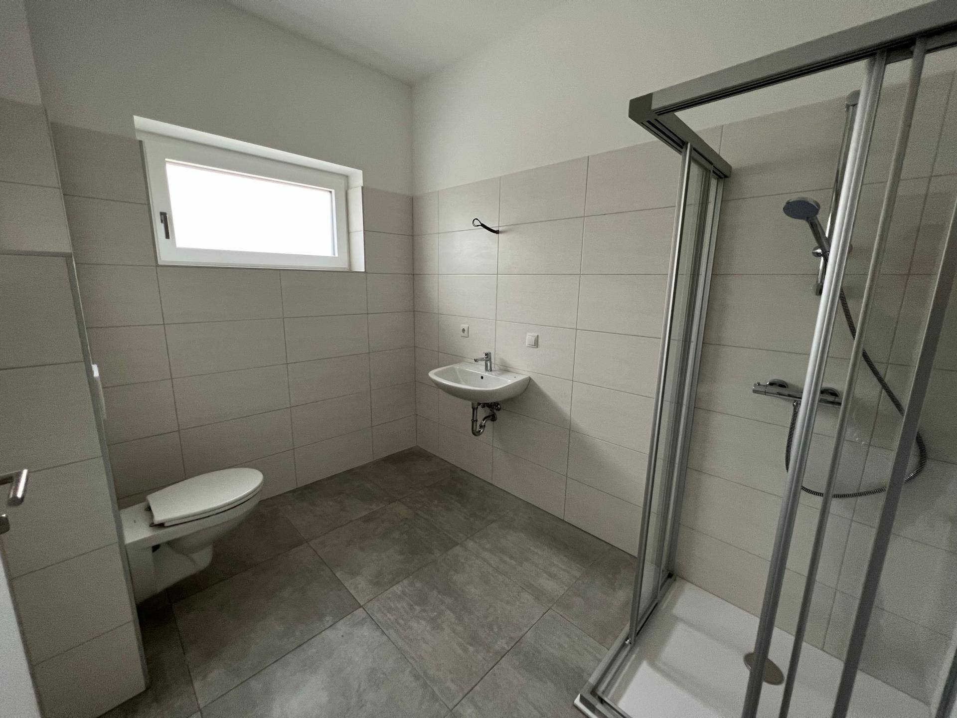 Modernes Badezimmer mit Duschkabine, WC, Waschbecken und Fenster für Tageslicht.