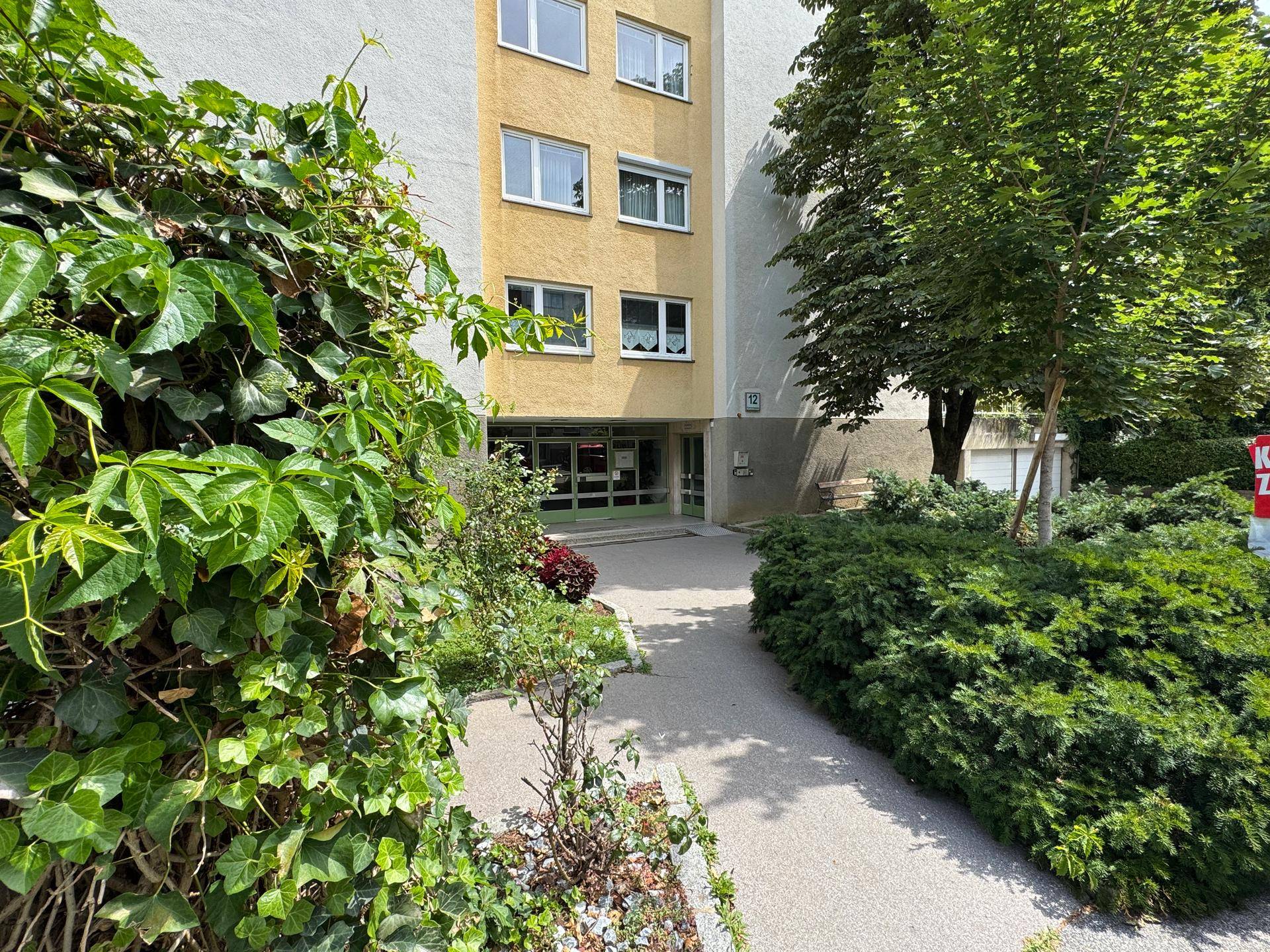 Eingangsbereich des Mehrfamilienhauses, umgeben von gepflegten Sträuchern und Pflanzen.