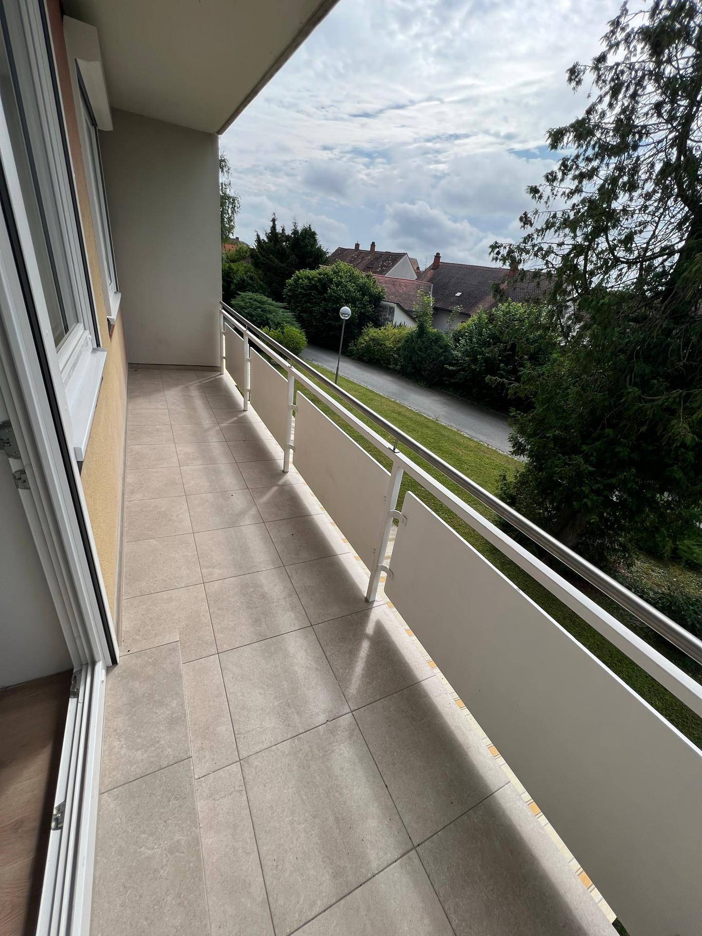 Geräumiger Balkon mit Fliesenboden und Blick auf die grüne Umgebung und Häuser.