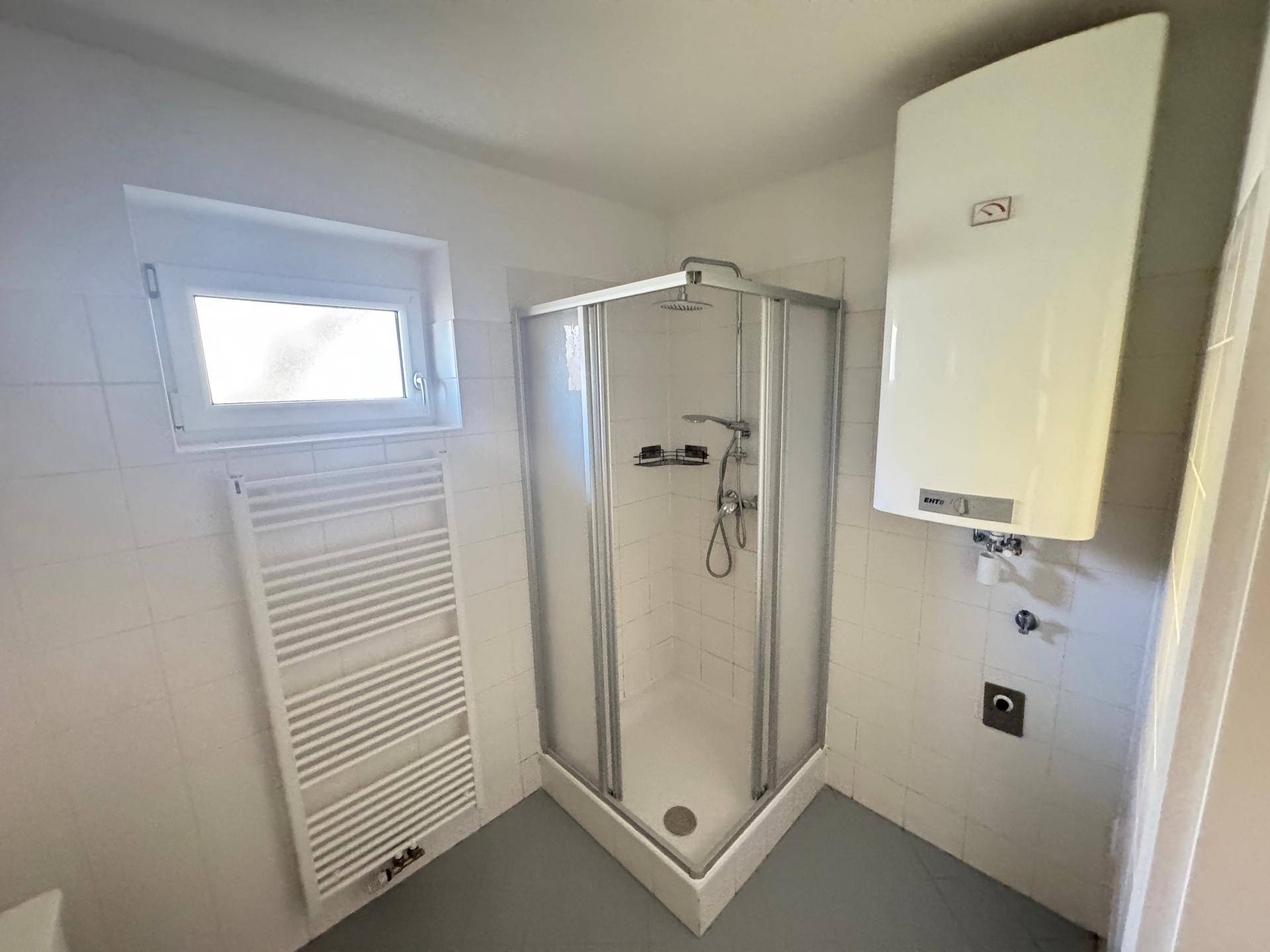 Badezimmer mit Duschkabine, beheiztem Handtuchhalter und Warmwasserboiler an der Wand.