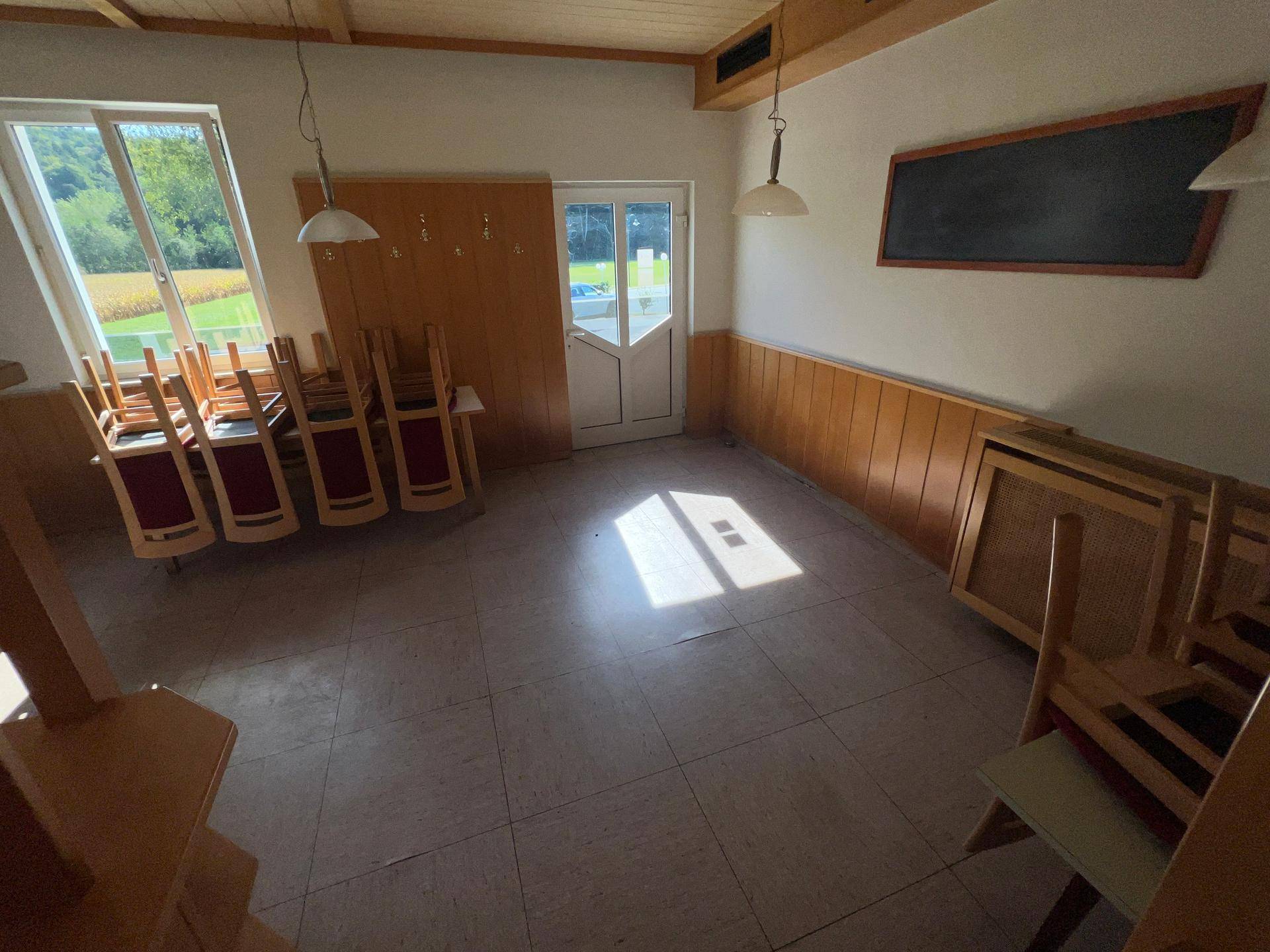 Heller Speisesaal mit Holztäfelung, Fliesenboden und Blick ins Grüne durch die Fenster.