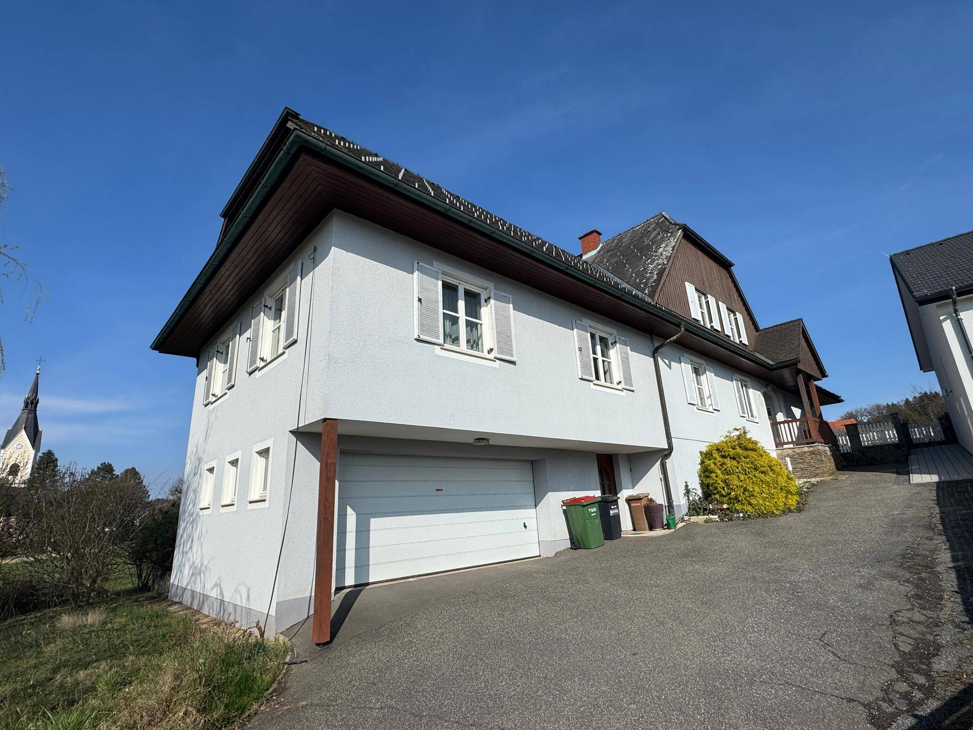 Seitenansicht des Hauses mit integrierter Garage und einem Kirchturm im Hintergrund.