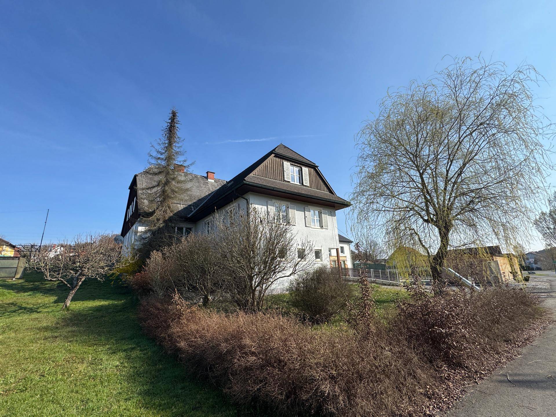 Freistehendes Haus mit Mansarddach und weitläufiger Grünfläche unter strahlend blauem Himmel.