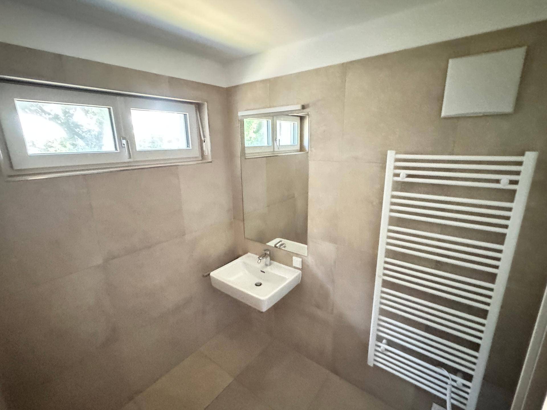 Helles Badezimmer mit Fenster, Waschbecken, Spiegel und beheiztem Handtuchhalter.