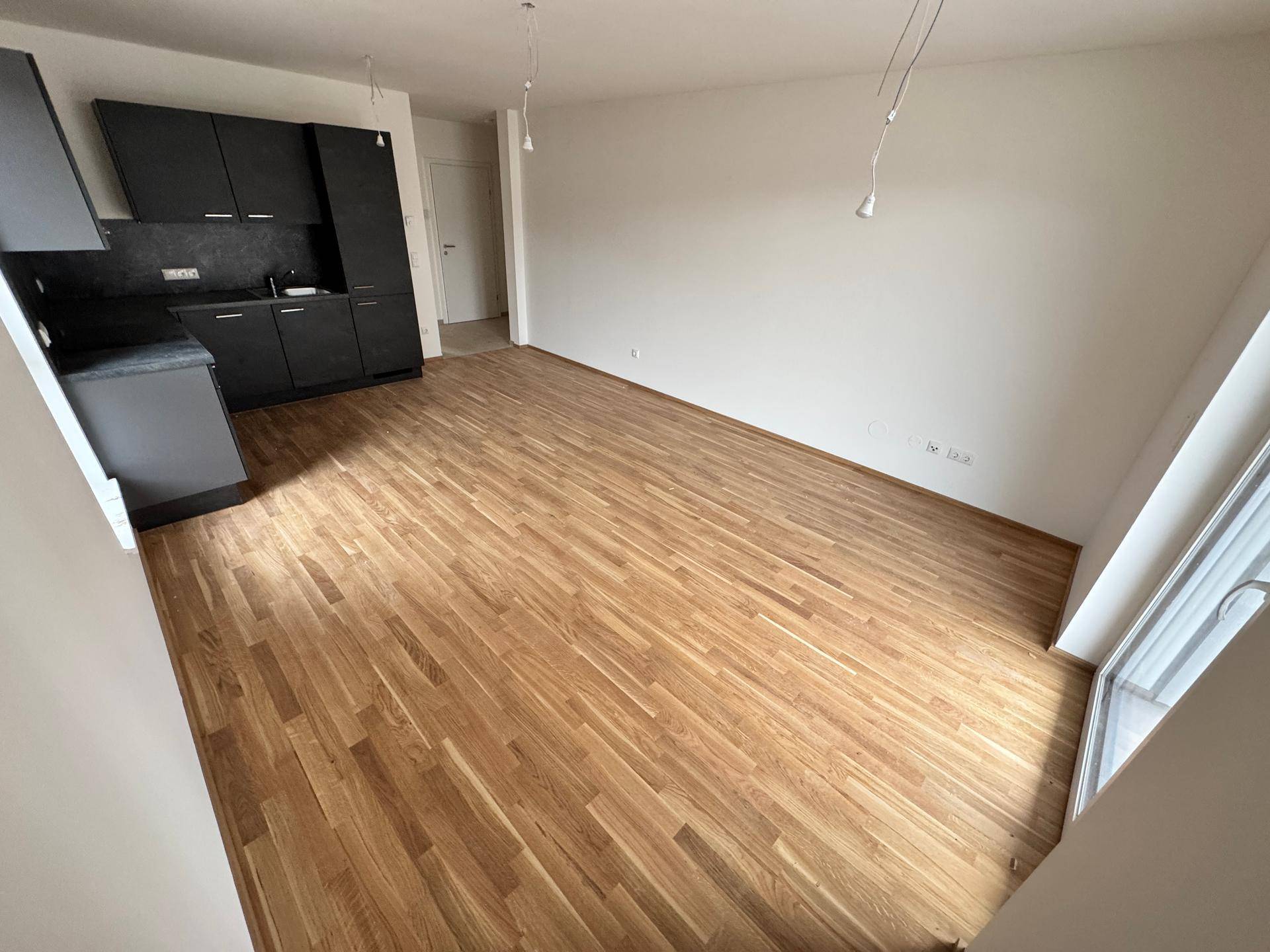 Geräumiger Wohn-Essbereich mit dunkler Küchenzeile und hellem Parkettboden, ideal für offenes Wohnen.