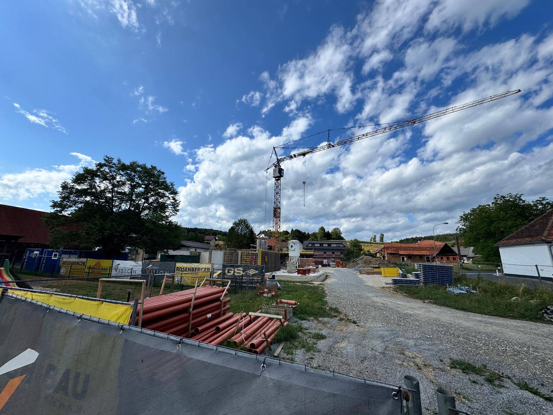 Übersicht der Baustelle mit Kran, Rohren und weiteren Baumaterialien im ländlichen Umfeld.