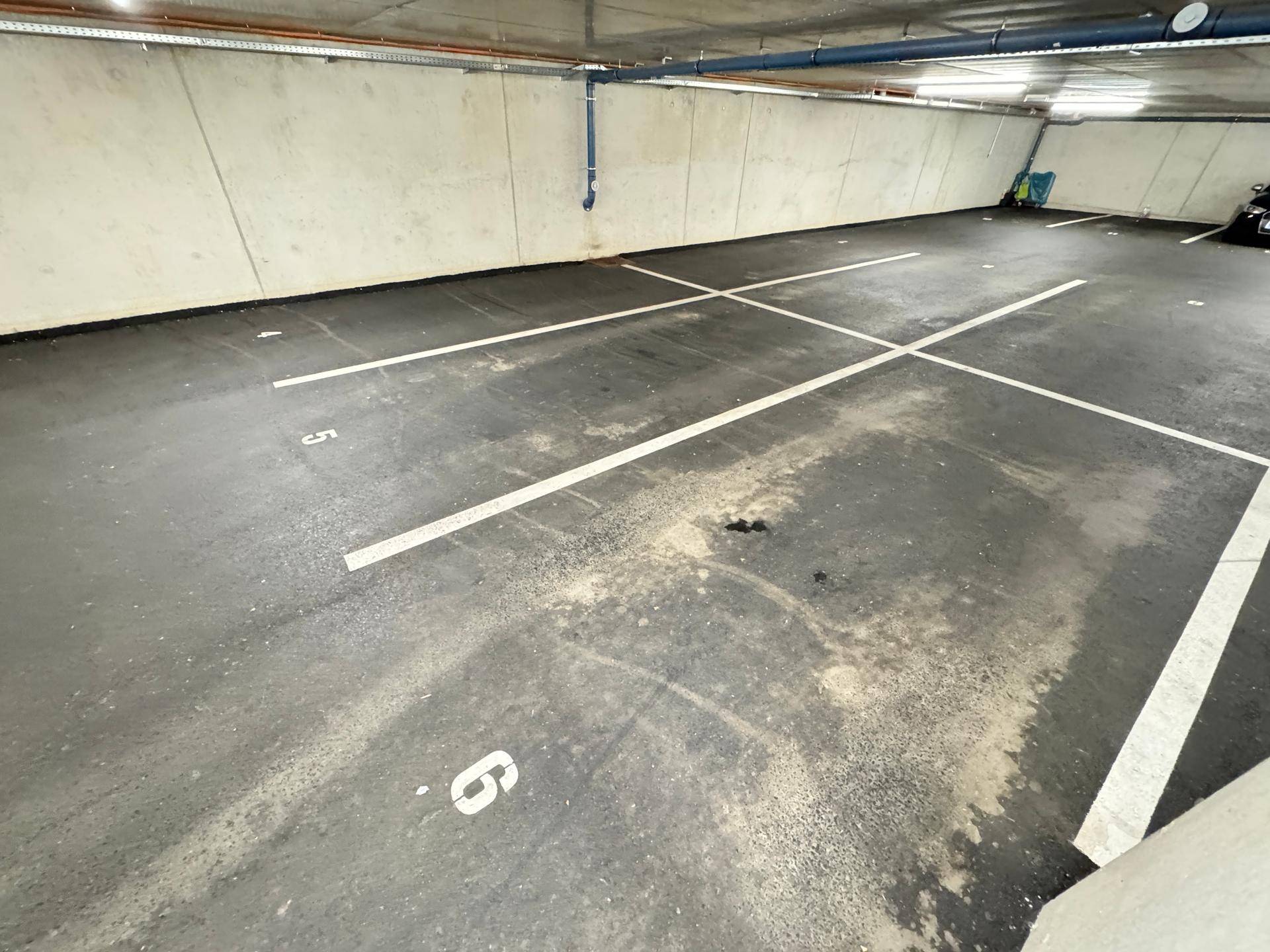 Tiefgarage mit markierten Stellplätzen auf asphaltiertem Boden und Betonwänden.