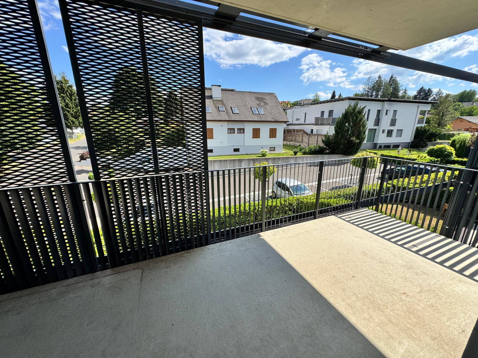 Heller Balkon mit modernem schwarzen Geländer und Blick auf die umliegenden Häuser und die Natur.