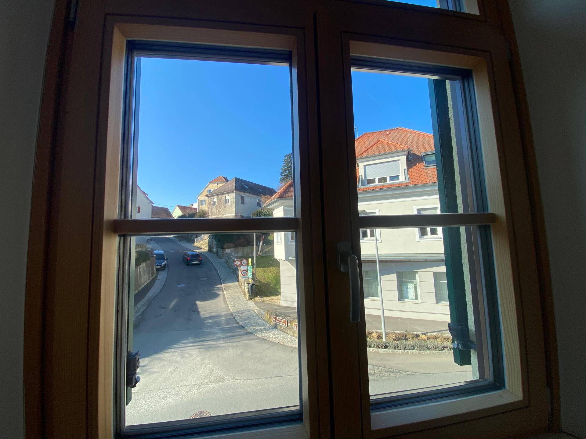 Blick aus einem Holzfenster auf eine ruhige Wohnstraße mit gepflegten Häusern.