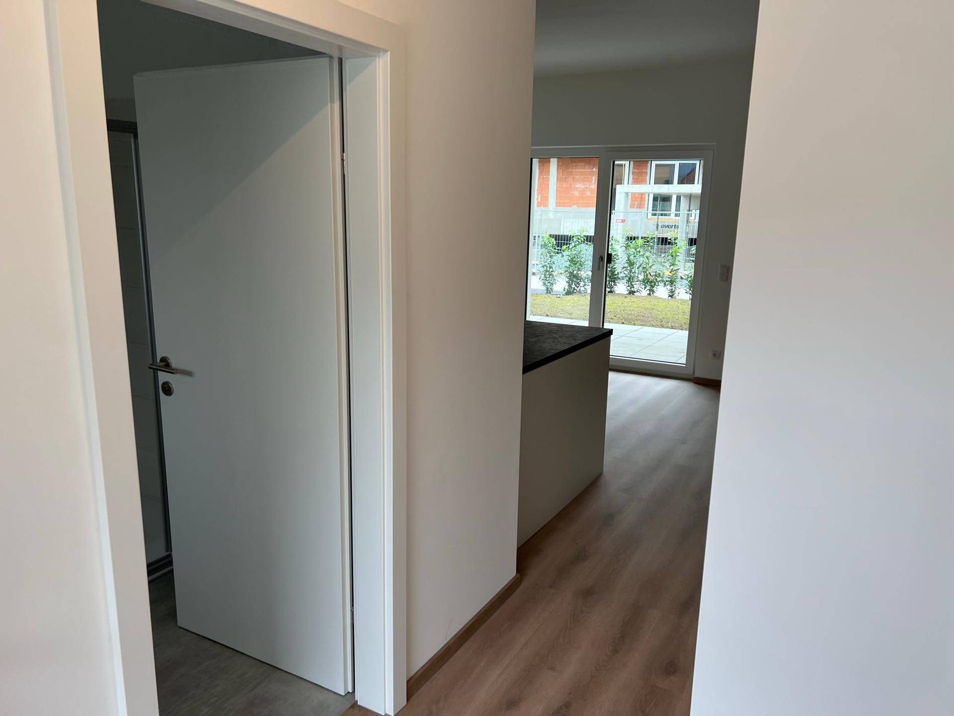 Heller Flur mit Laminatboden, der zu einem offenen Wohnbereich mit Gartenzugang führt.