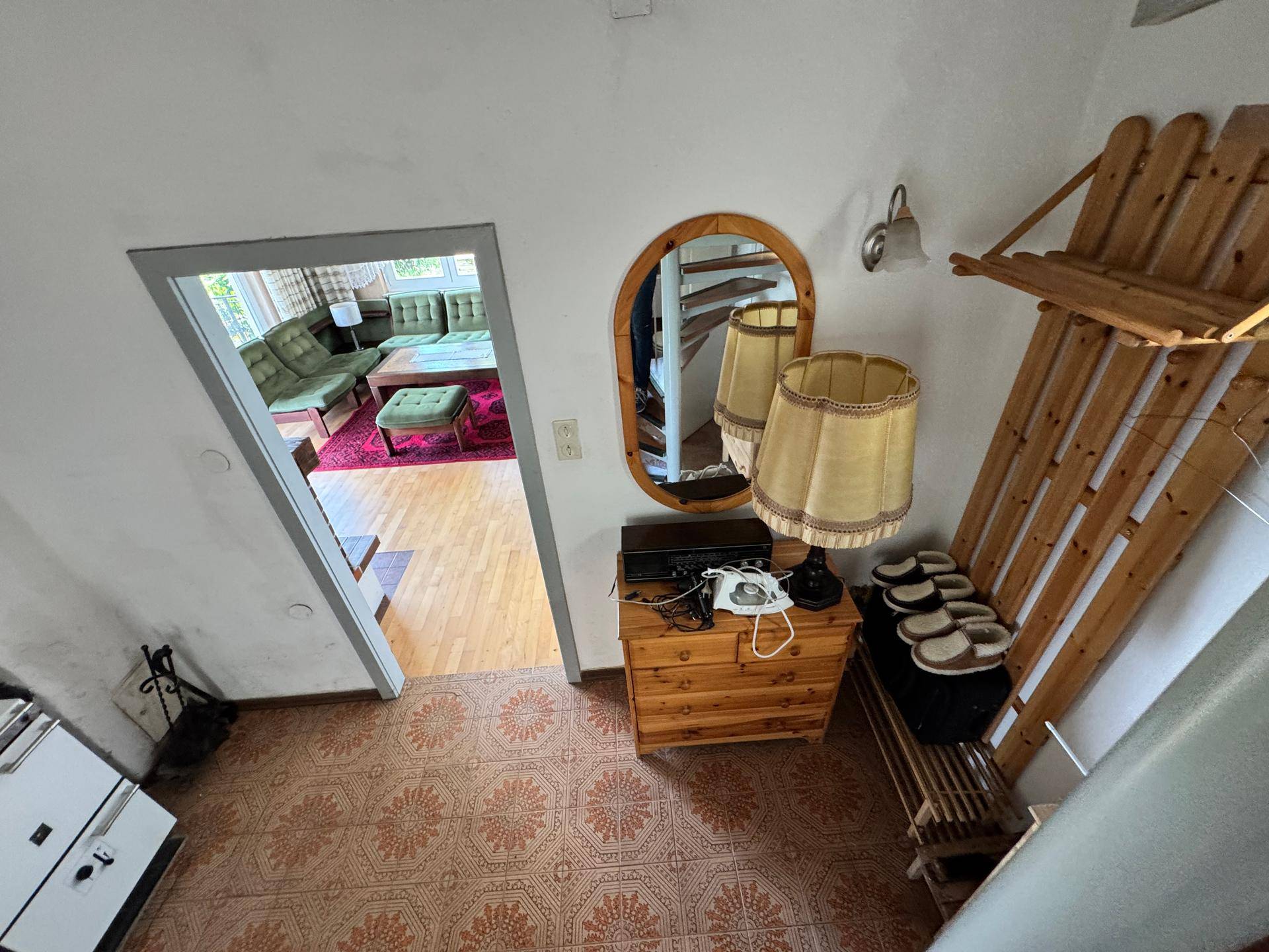 Eingangsbereich mit gemustertem Boden, Holzmöbeln und Blick in das Wohnzimmer.