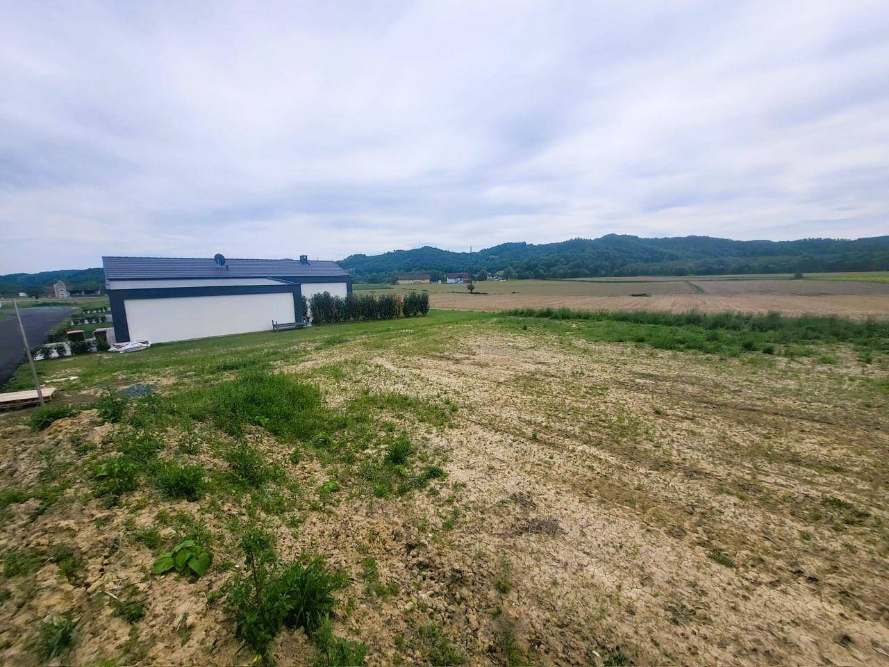 Weitläufige Landschaft mit Feldern und einem modernen Haus am Horizont.