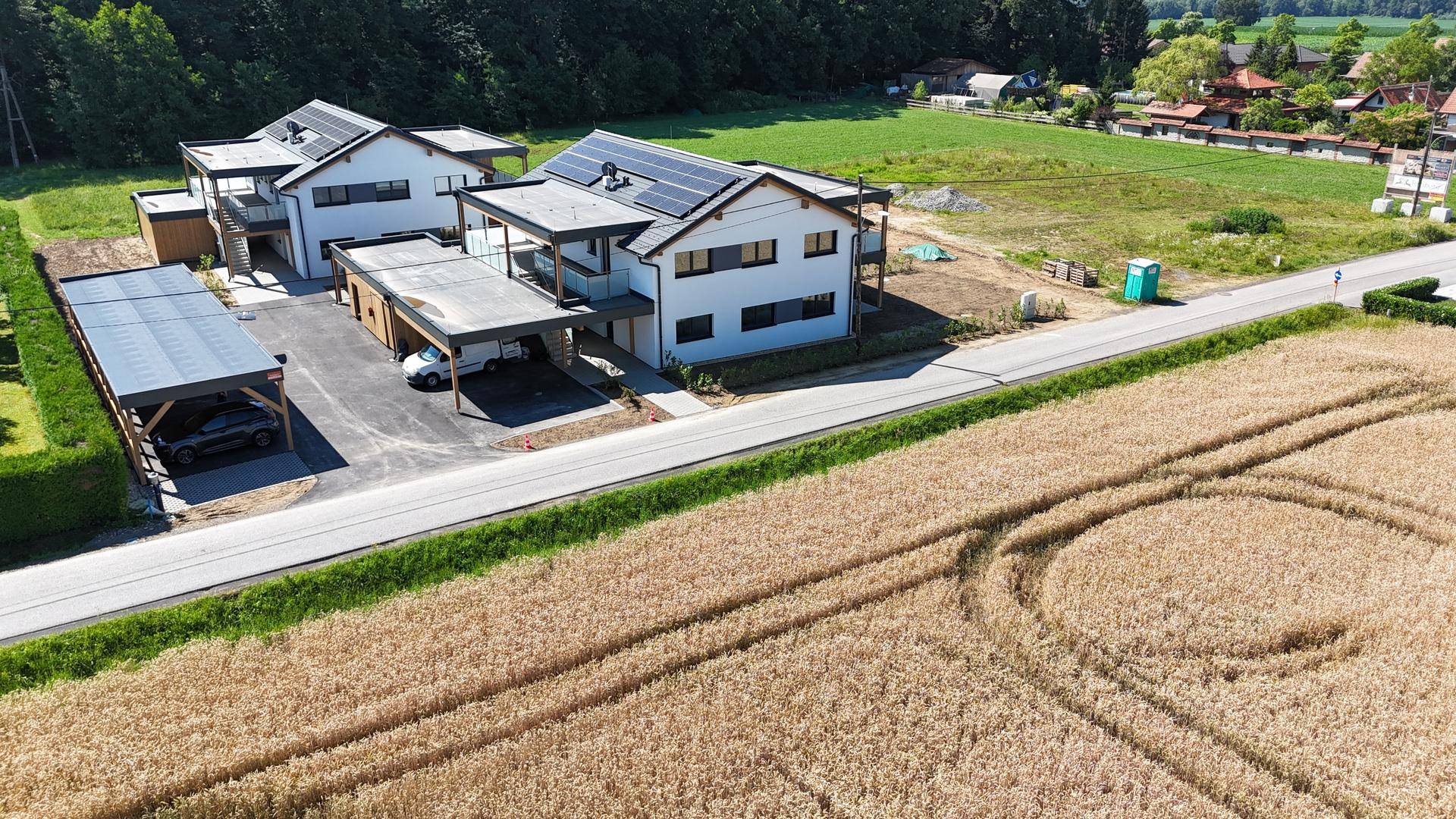 Luftaufnahme von zwei modernen Doppelhaushälften mit Carports und Solaranlagen an einer Landstraße.