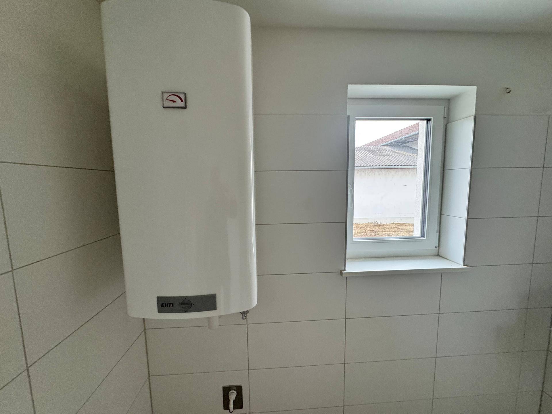 Kleiner Hauswirtschaftsraum mit Warmwasserboiler und Fenster, ideal für Technik und Lagerung.
