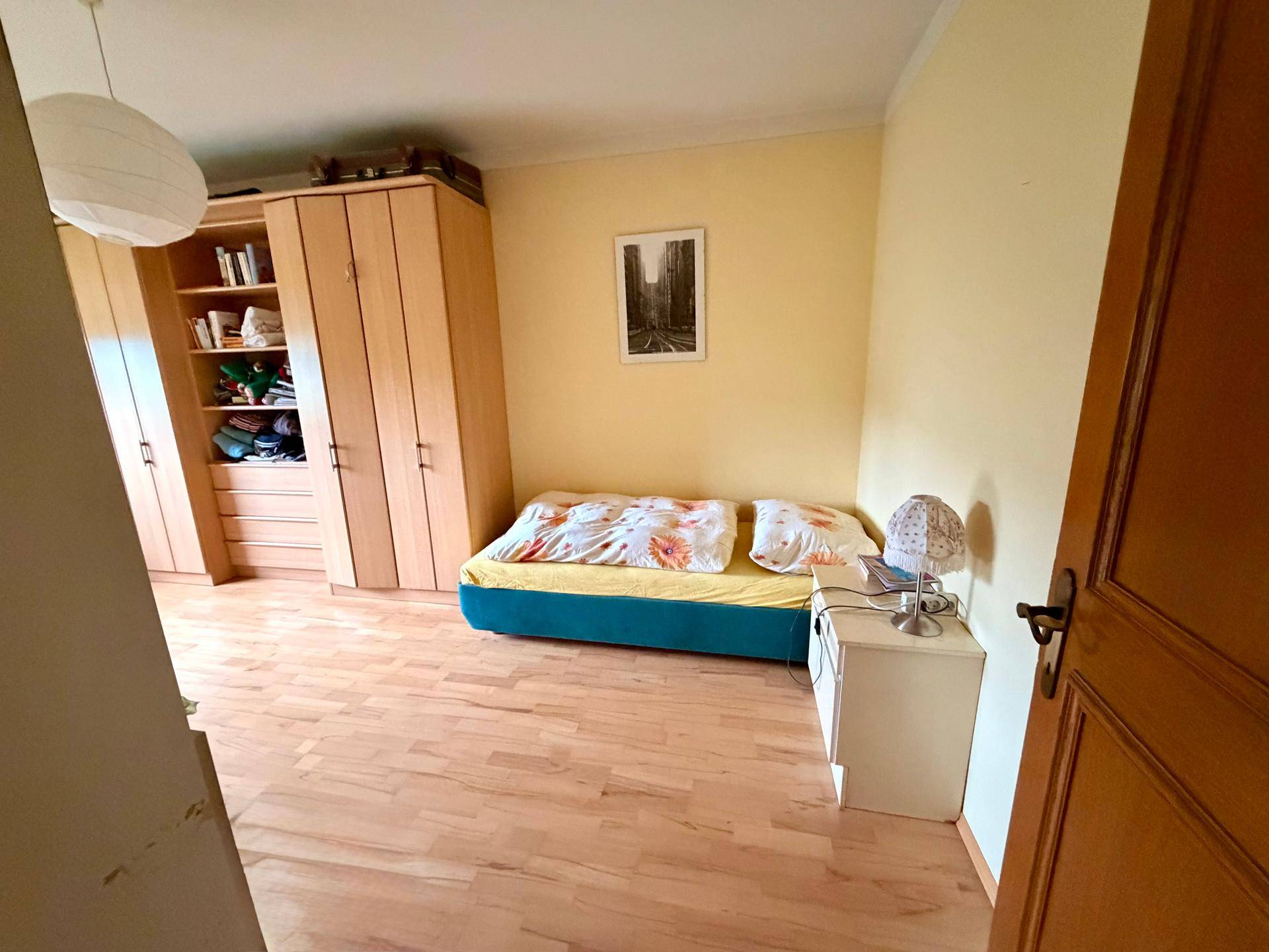 Helles Schlafzimmer mit Einzelbett, Holzschränken und Blick ins Grüne.