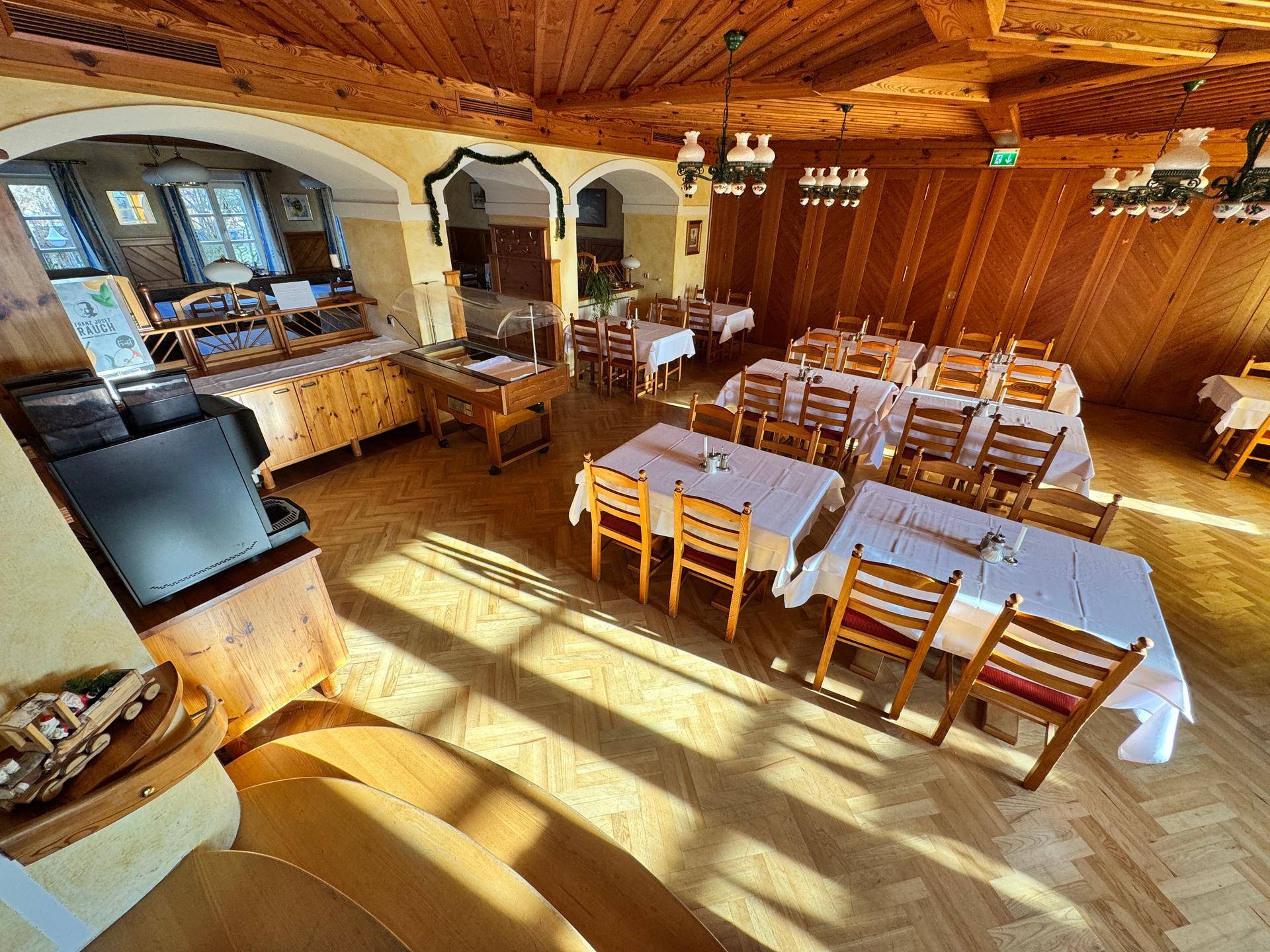 Heller Speisesaal mit Holzbalkendecke, gedeckten Tischen und viel Tageslicht.