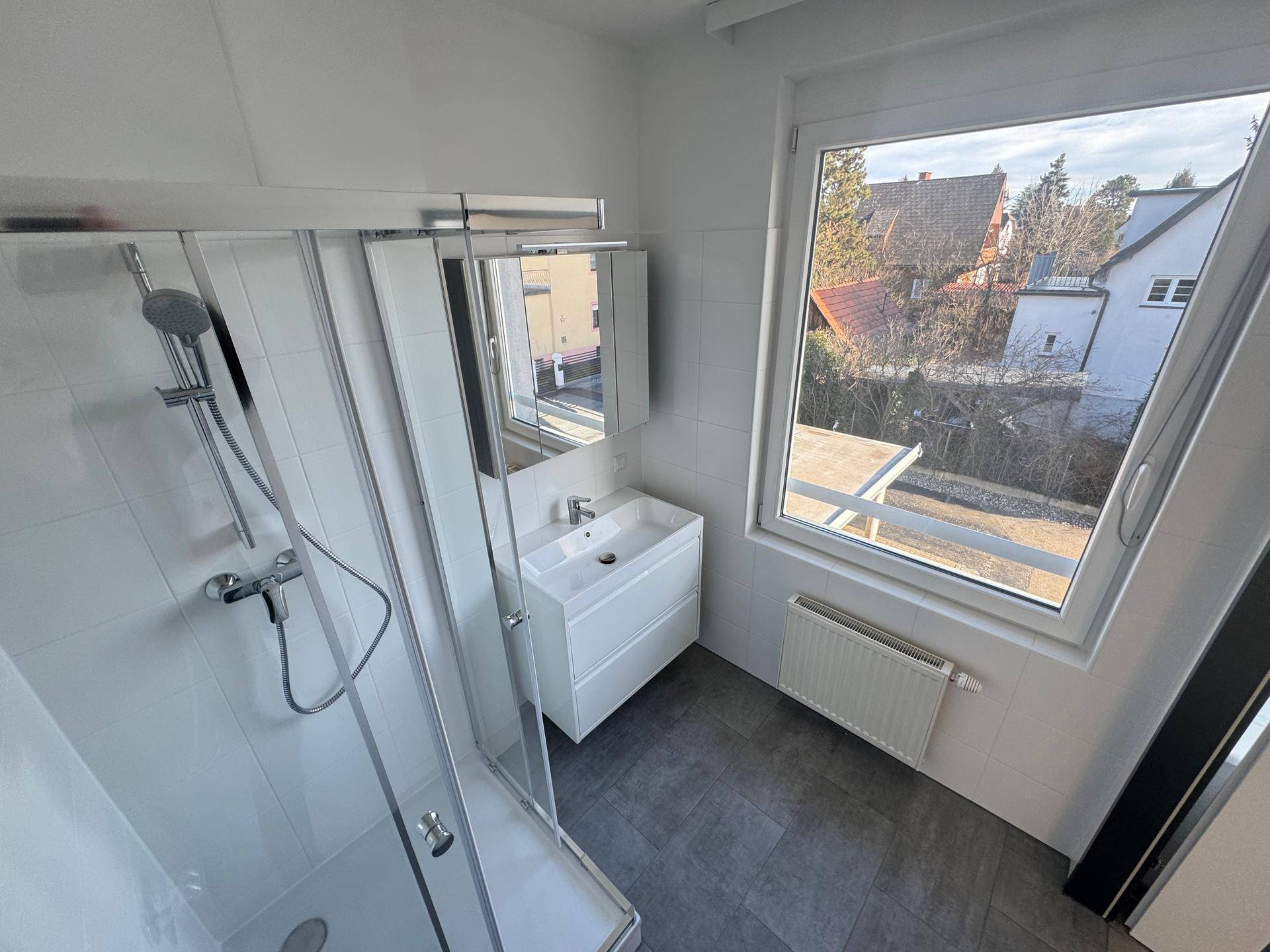 Modernes Badezimmer mit Dusche, Waschbecken und Fenster mit Ausblick.