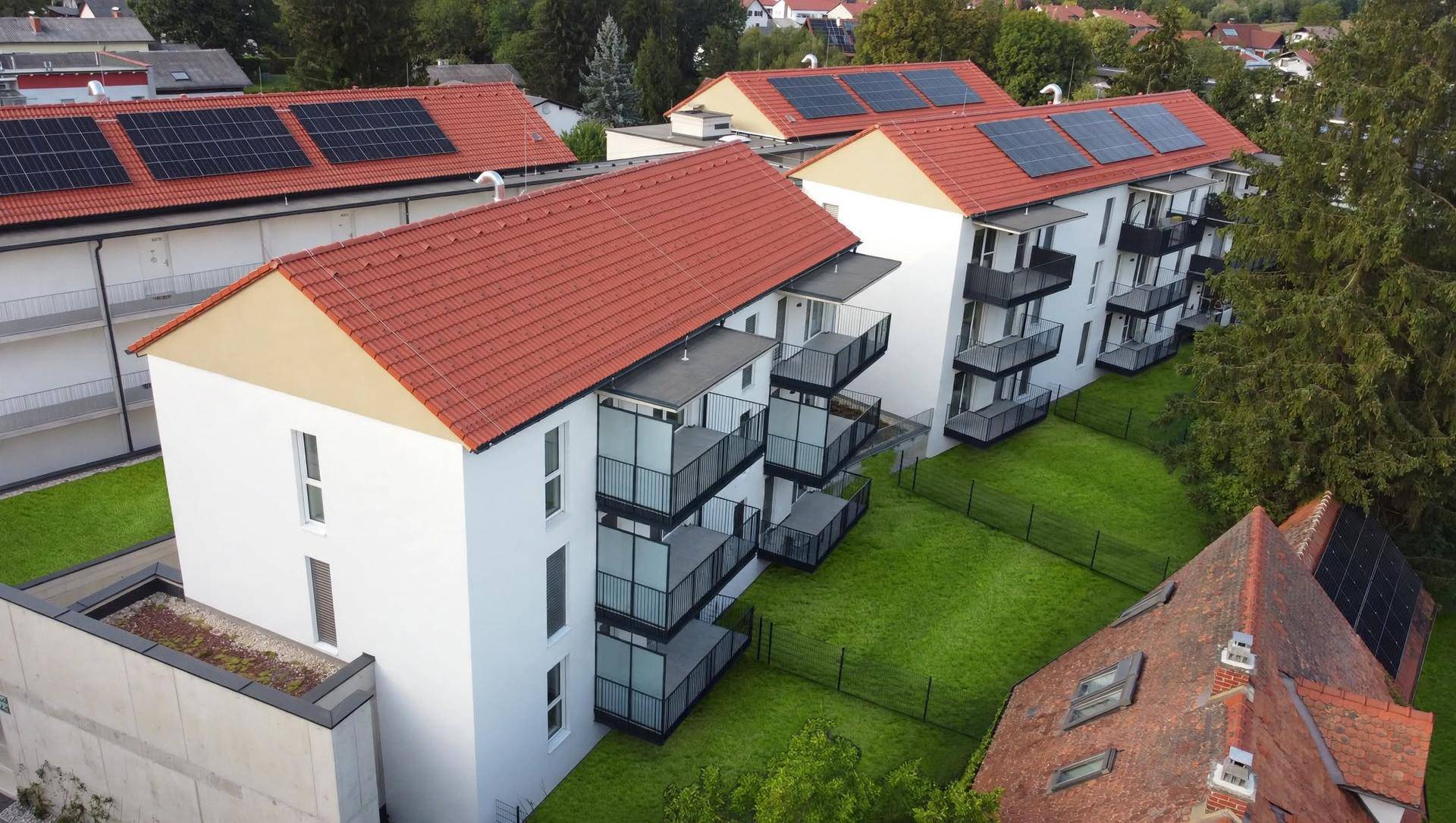 Nahaufnahme des modernen Wohnkomplexes mit weißen Fassaden, schwarzen Balkonen und Solaranlagen auf den Dächern.
