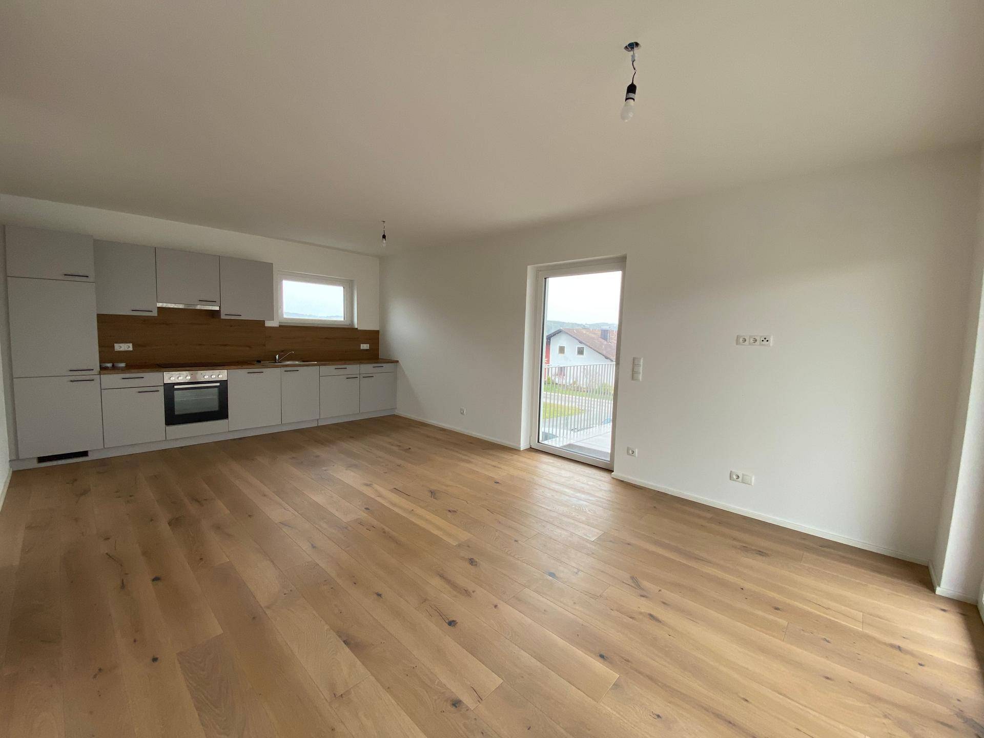 Offener Wohn- und Essbereich mit integrierter Küche, Holzboden und Zugang zum Balkon.