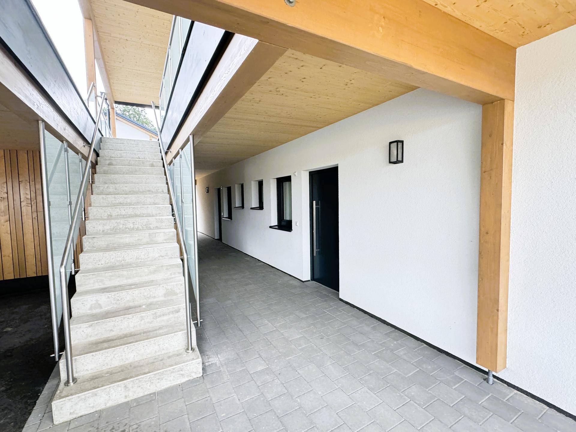 Überdachter Außenflur mit Treppe und Zugang zu den Wohnungen in einem Neubau.