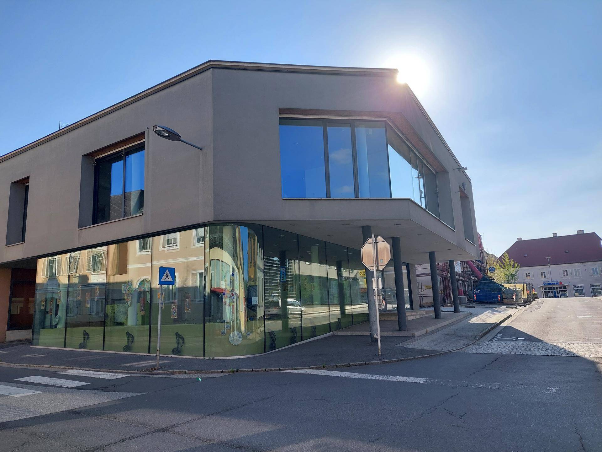 Eckansicht des modernen Gebäudes mit geschwungener Glasfassade und viel Sonnenlicht.