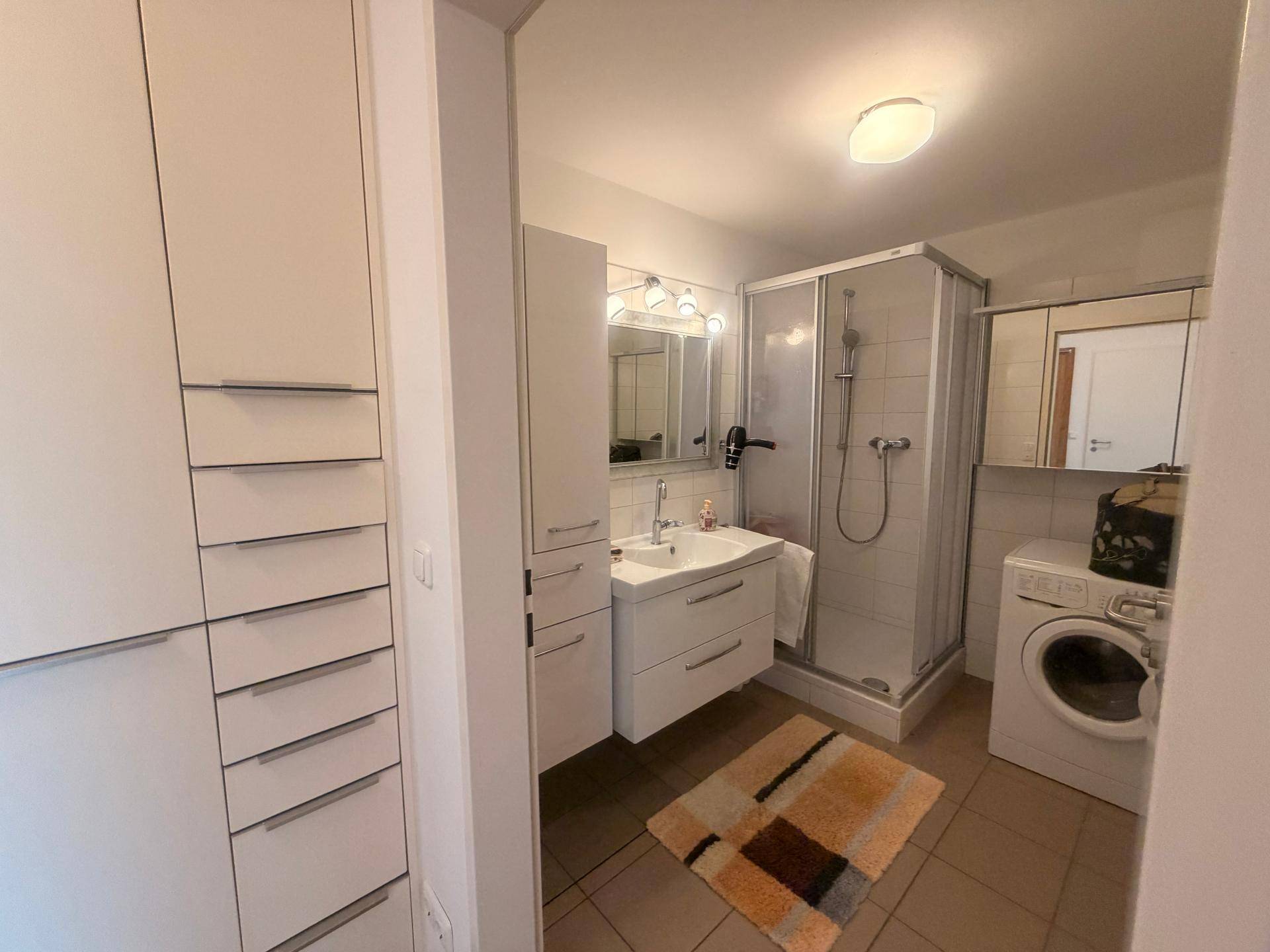 Badezimmer mit Duschkabine, Waschbecken, Spiegel und integrierter Waschmaschine.
